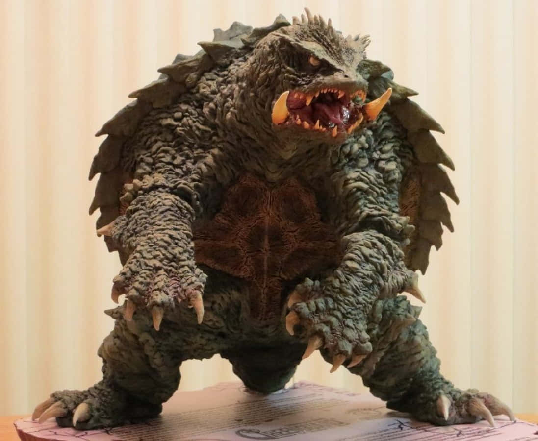 Gamera 桌布 壁紙 — 一個細節豐富的怪物雕像，背部有尖刺和鋒利的爪子，在柔和的米色窗簾背景下，威風凜凜地站在展示底座上。
