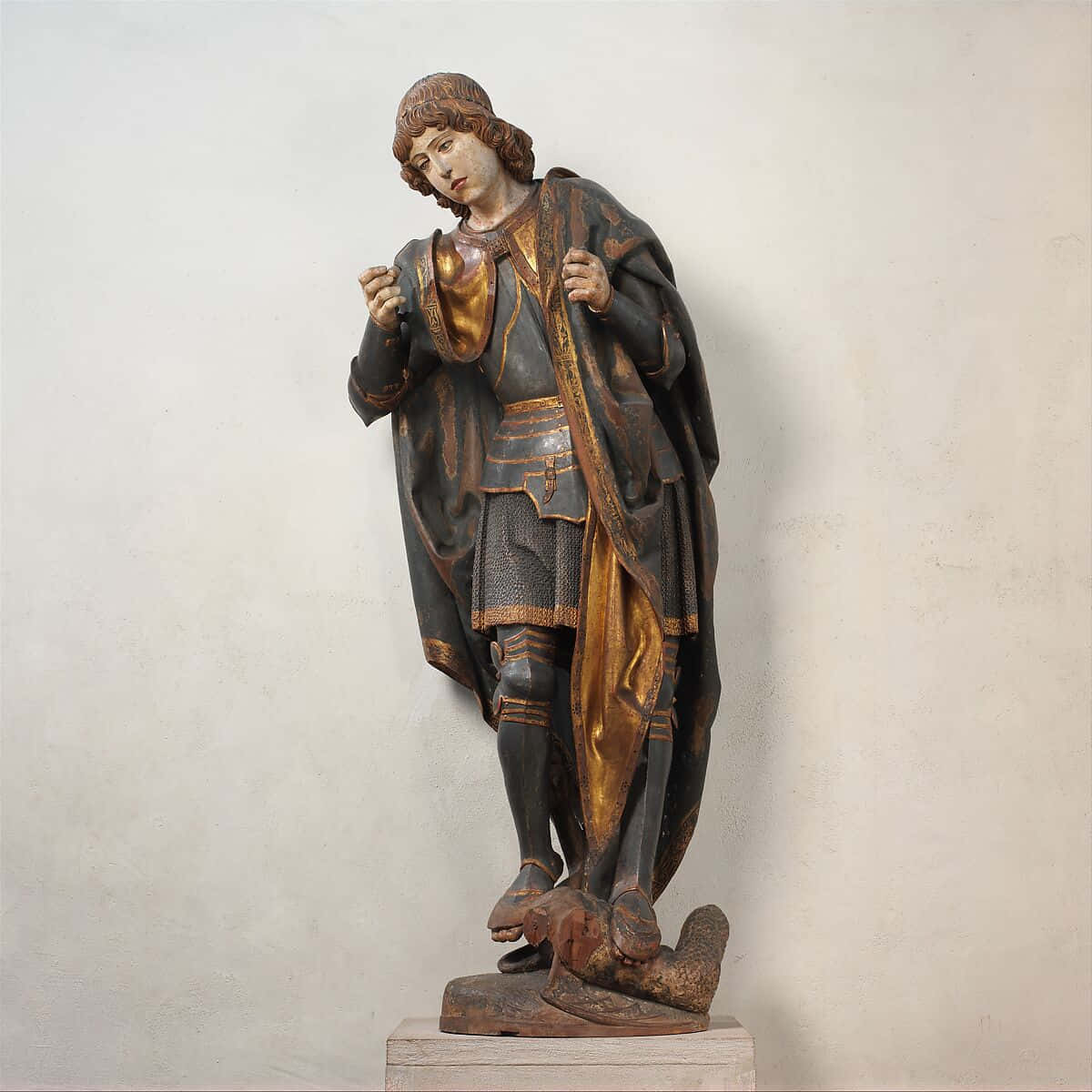 Saint Michael 桌布 壁紙 — 一個細節豐富的木製騎士雕像，身穿帶有金色裝飾的盔甲，莊嚴地站在素牆前。