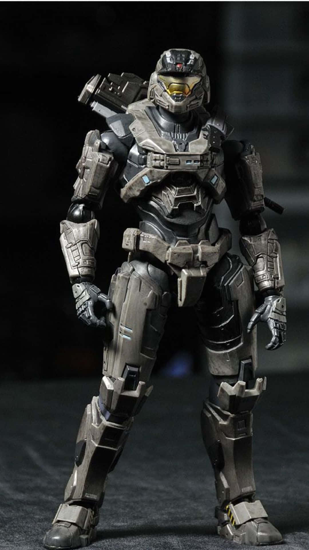 Noble Six 桌布 壁紙 — 一個細節豐富的灰黑色裝甲士兵人偶，在黑暗背景下擺出姿勢，帶有發光的黃色護目鏡。