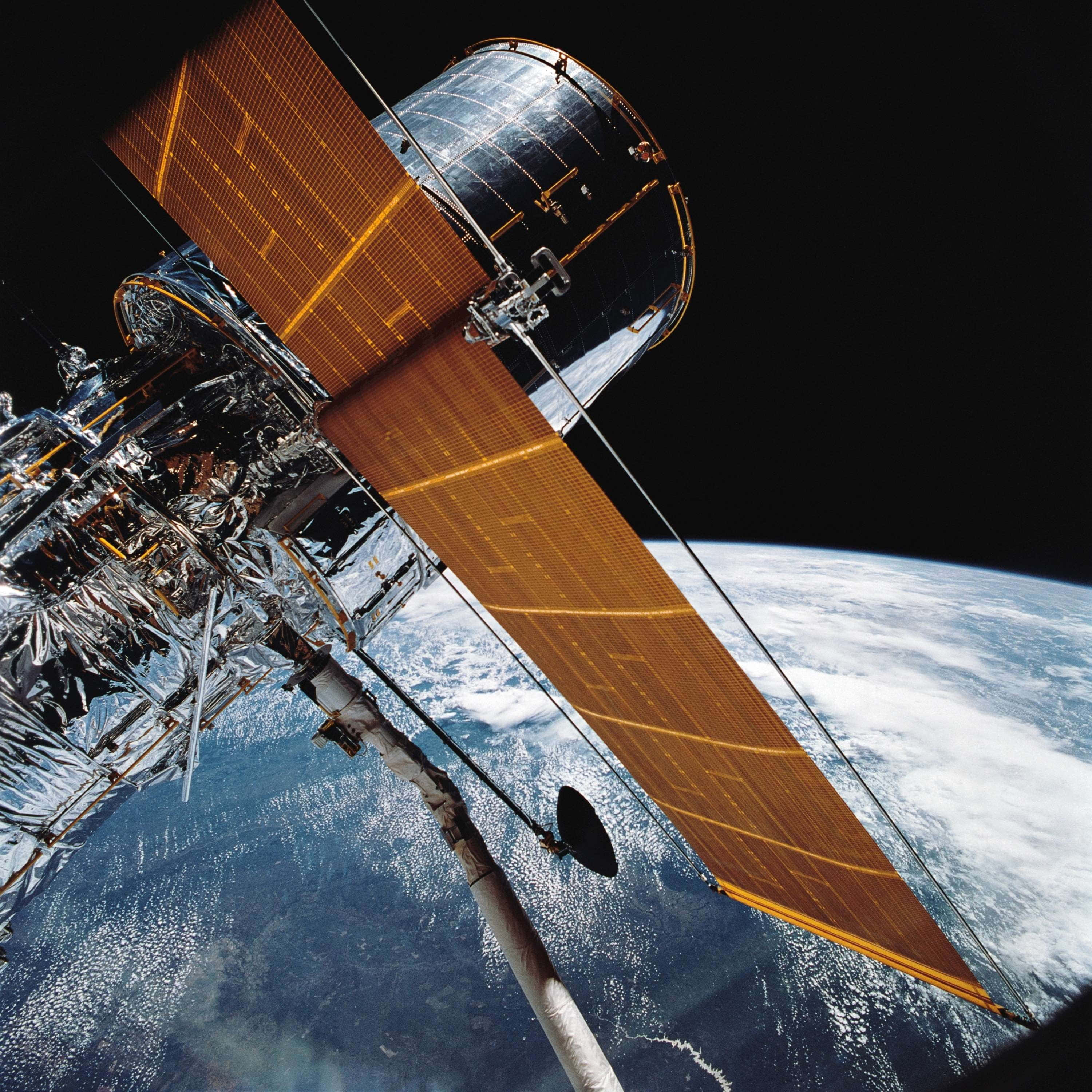 Space Technology 桌布 壁紙 — 一個細節豐富的衛星，帶有金色太陽能板，在太空的黑暗中繞地球運行。