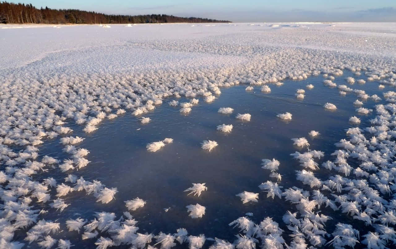 Frozen Lake 桌布 壁紙 — 一個結冰的湖泊，覆蓋著複雜的白色冰晶，在蒼白的天空下，一條深藍色的融水池蜿蜒穿過中心。