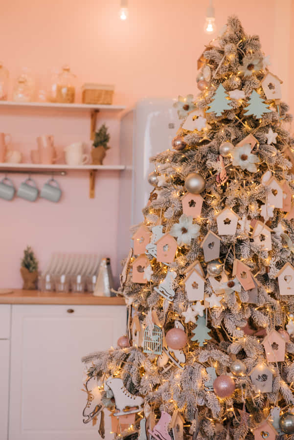 Aesthetic Christmas Tree 桌布 壁紙 — 一個結霜的聖誕樹，裝飾著粉彩鳥屋和閃閃發光的飾品，在粉紅色的廚房裡溫暖地發光。