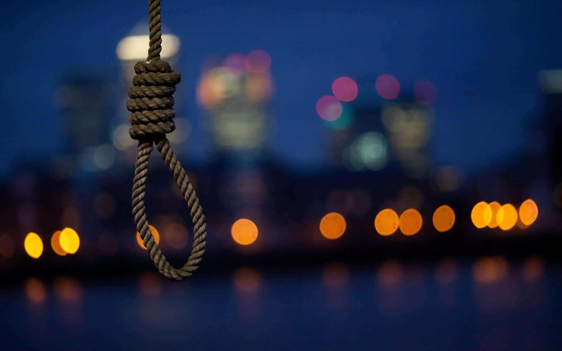 自殺 桌布 壁紙 — 一個絞索在夜間模糊的城市天際線背景下清晰對焦，散景燈光在水面上反射。