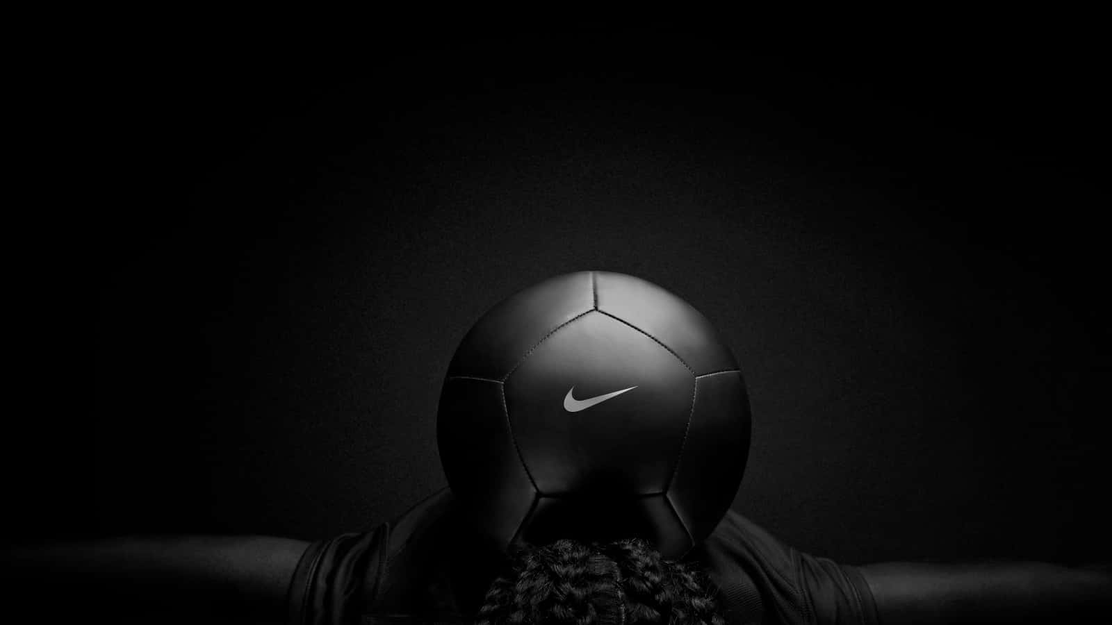 Soccer Ball 桌布 壁紙 — 一個綁辮子的人在黑暗背景前將一個黑色Nike足球舉過頭頂。