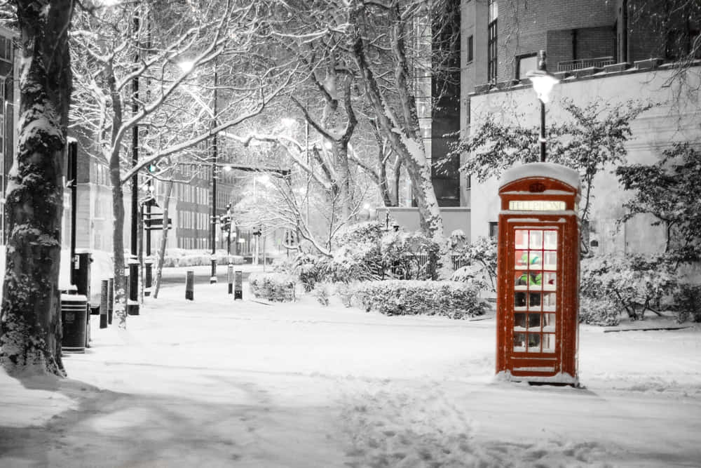 Snow 4K 桌布 壁紙 — 一個經典的紅色電話亭獨自矗立在積雪的城市街道上，夜晚中溫暖地發光，與單色的冬季場景形成對比。