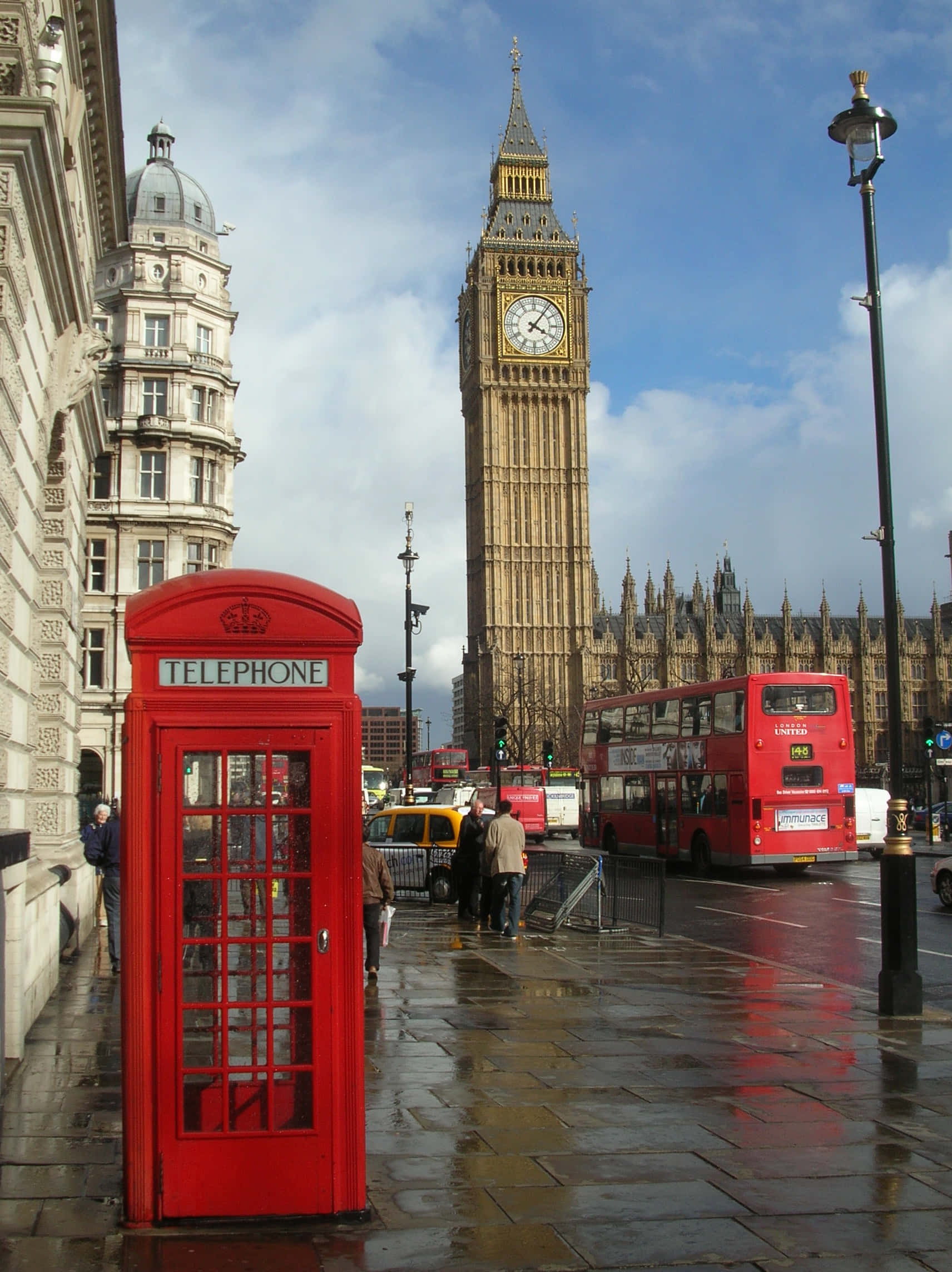 London iPhone 桌布 壁紙 — 一個經典的紅色電話亭矗立在濕漉漉的倫敦街道上，大笨鐘在部分多雲的天空下聳立在背景中。