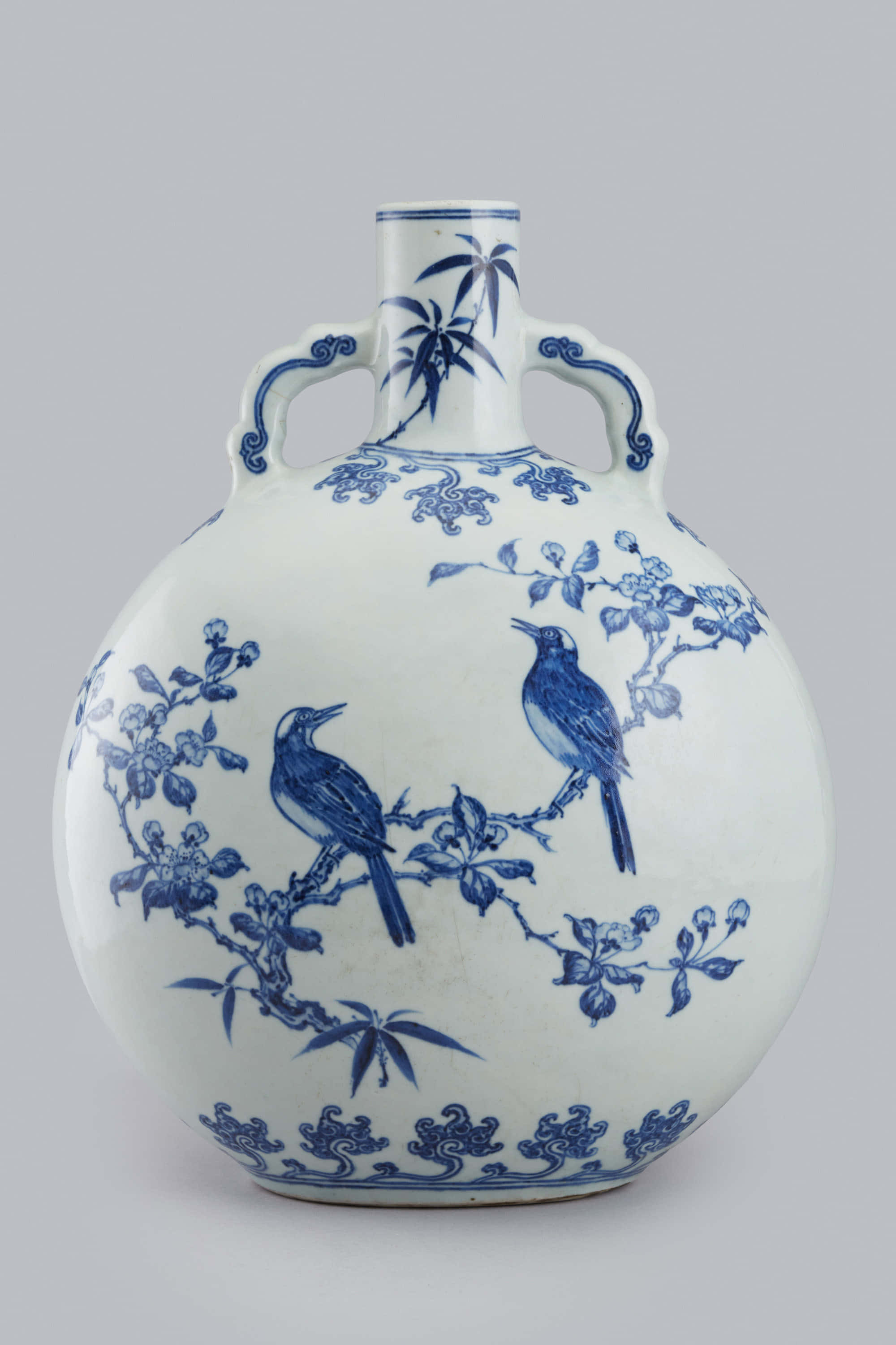 Ceramic 桌布 壁紙 — 一個經典的藍白瓷花瓶，有兩個把手，上面有精緻的手繪鳥兒棲息在開花的樹枝上。