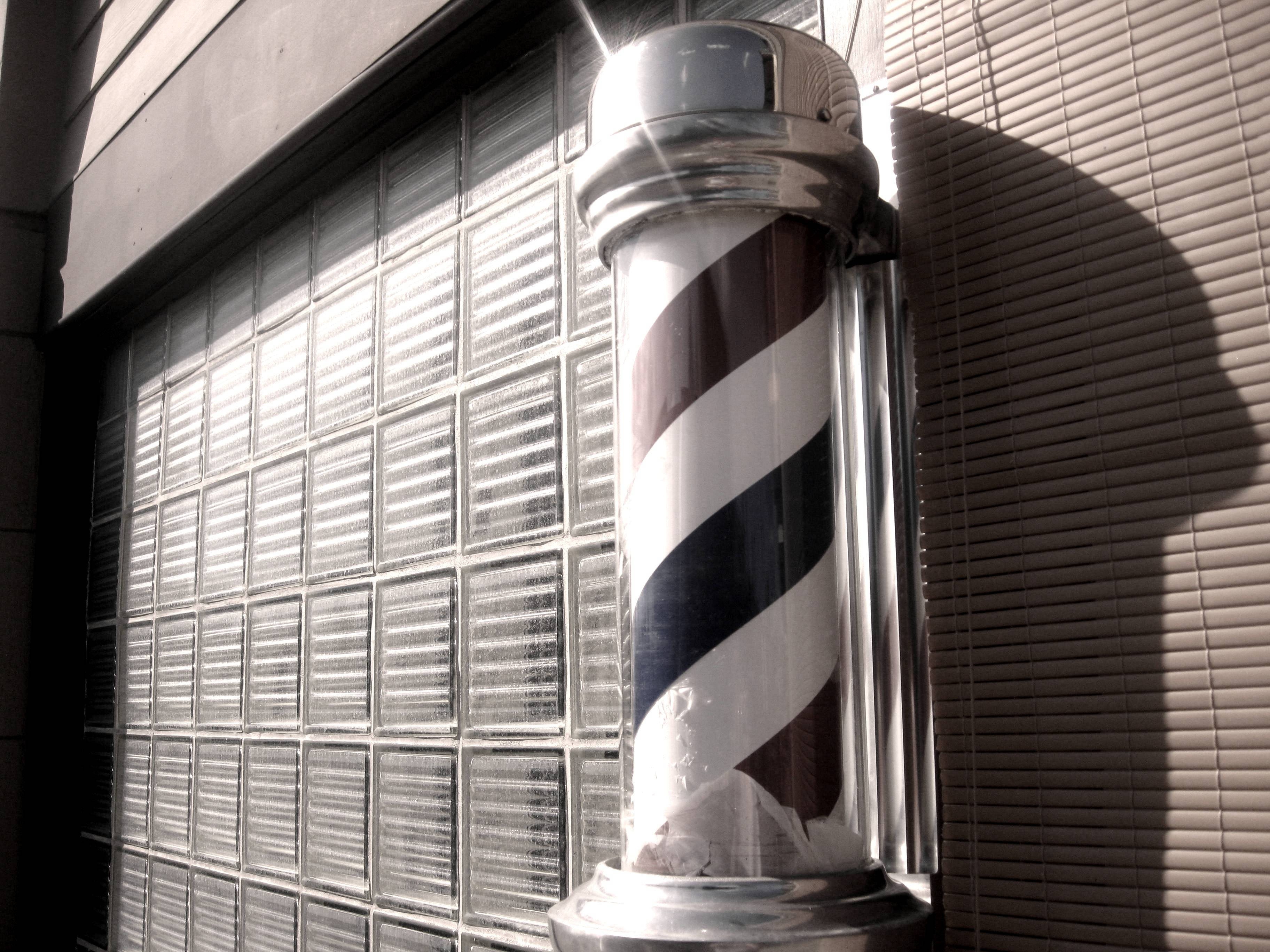 Barber 桌布 壁紙 — 一個經典的鍍鉻理髮柱，帶有黑白斜條紋，立在玻璃磚牆和竹百葉簾前。