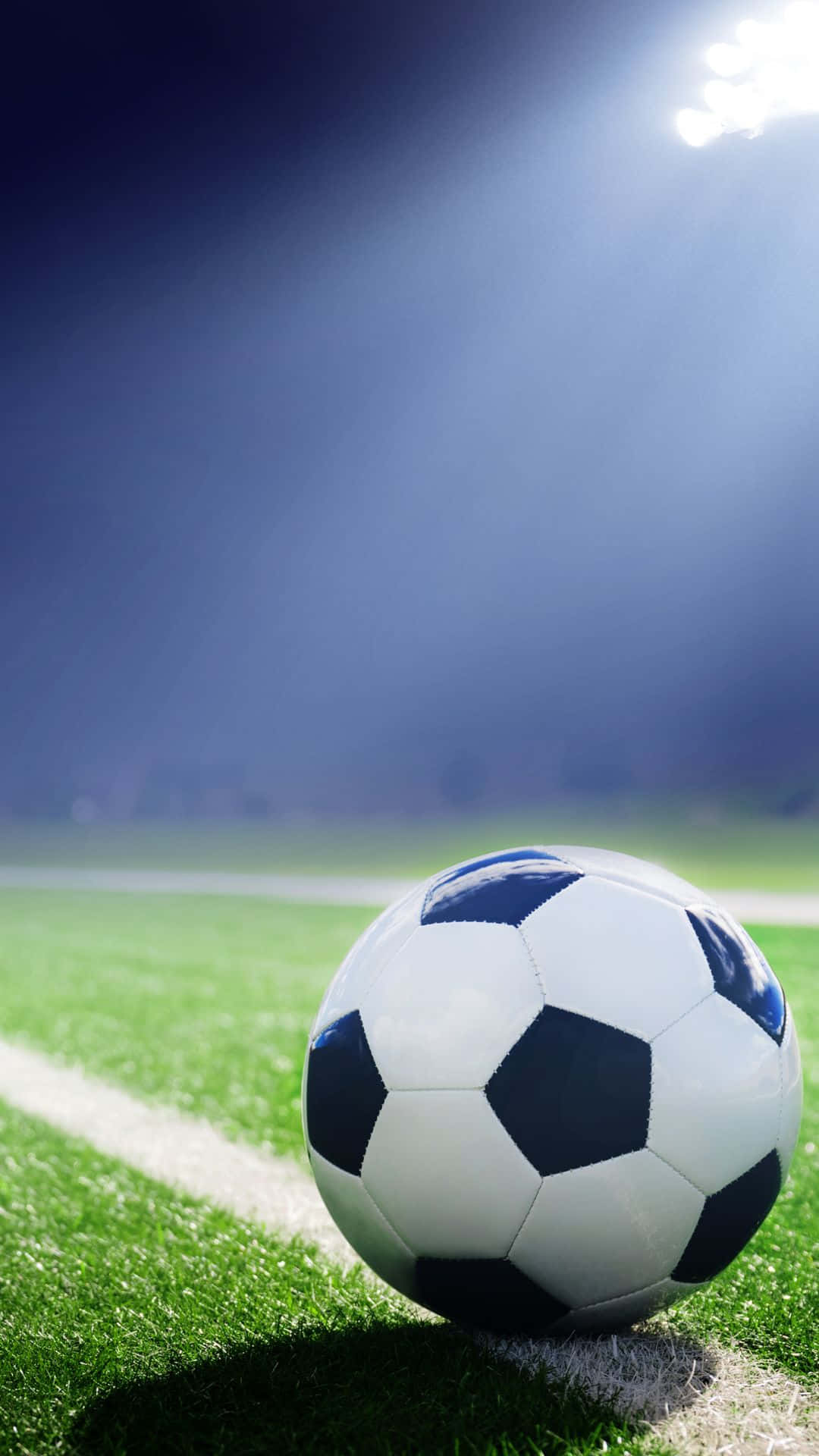 Soccer iPhone 桌布 壁紙 — 一個經典的黑白足球在明亮的球場燈光下，停留在充滿活力的綠色草地上。