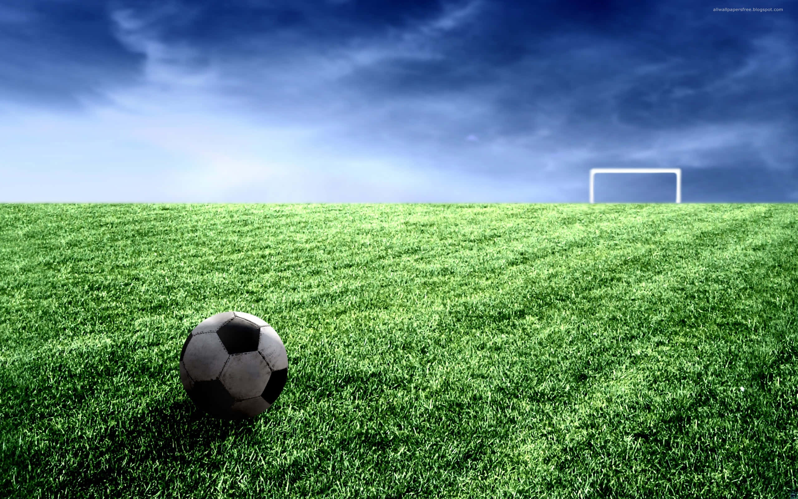 sport 桌布 壁紙 — 一個經典的黑白足球放在充滿活力的綠色草地上，遠處有白色的球門柱，背景是戲劇性的藍天。