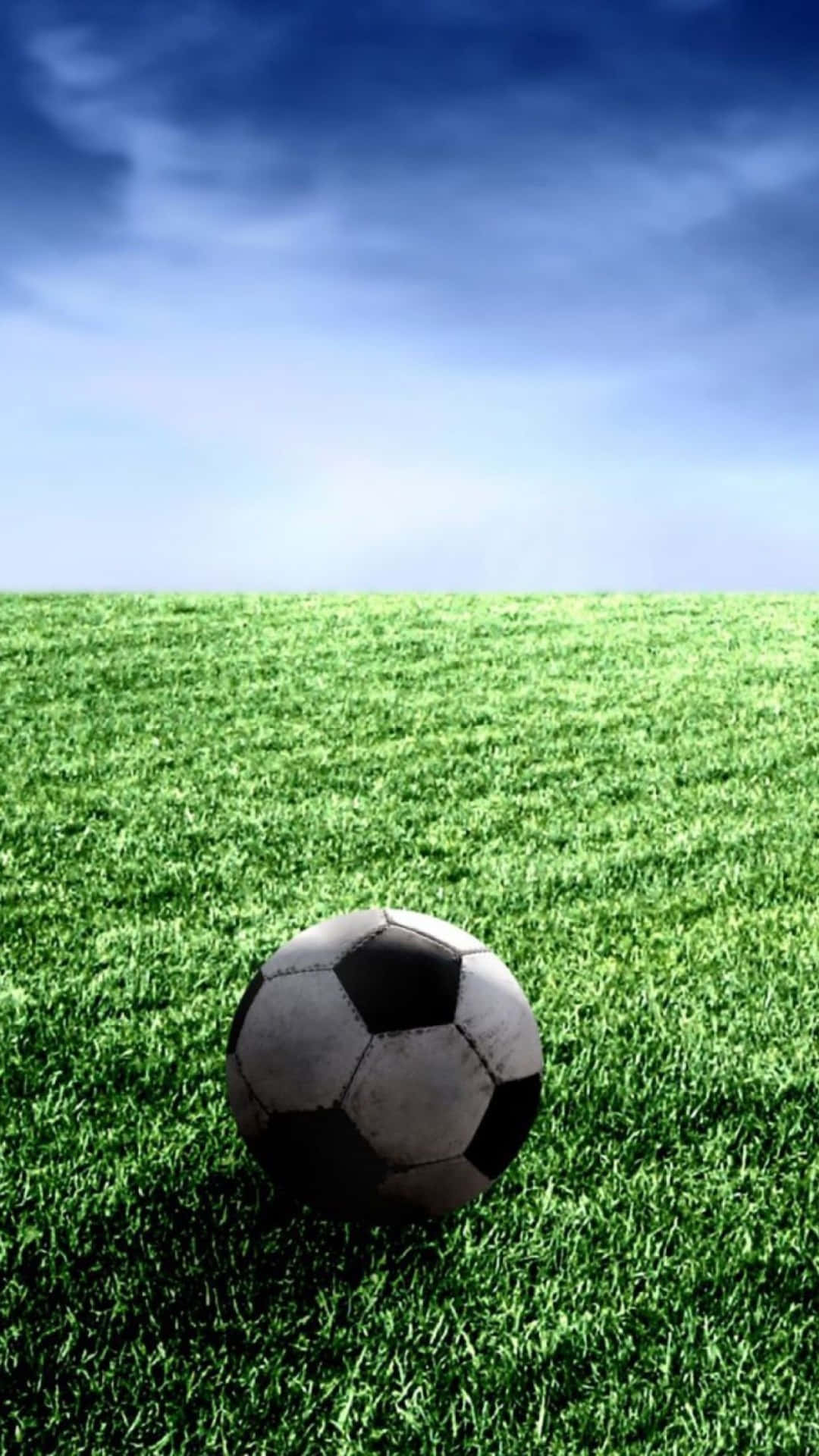 Soccer iPhone 桌布 壁紙 — 一個經典的黑白足球放在充滿活力的綠色草地上，廣闊的藍天上有柔軟的白雲。