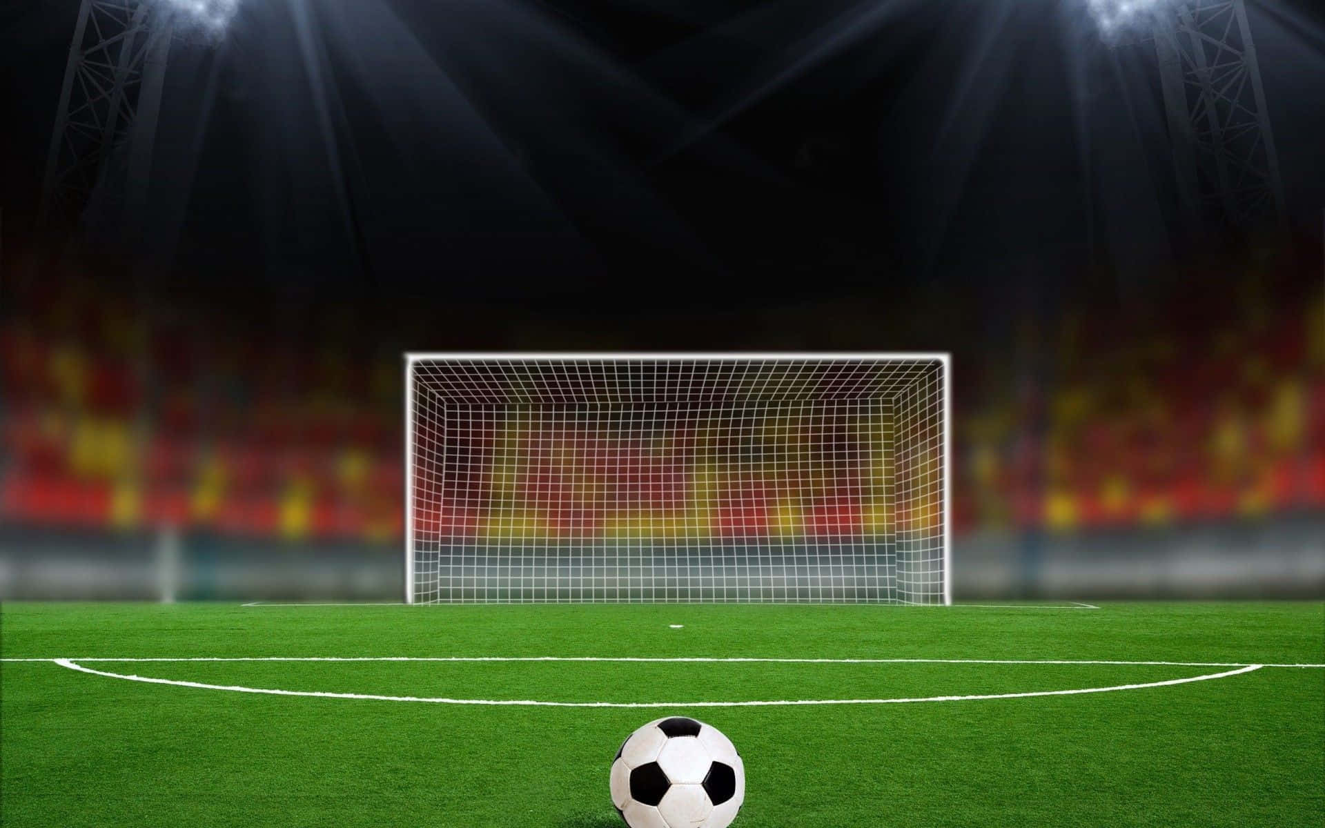 Football Field 桌布 壁紙 — 一個經典的黑白足球放在充滿活力的綠色草地上，前面是發光的體育場球門，在戲劇性的聚光燈下。