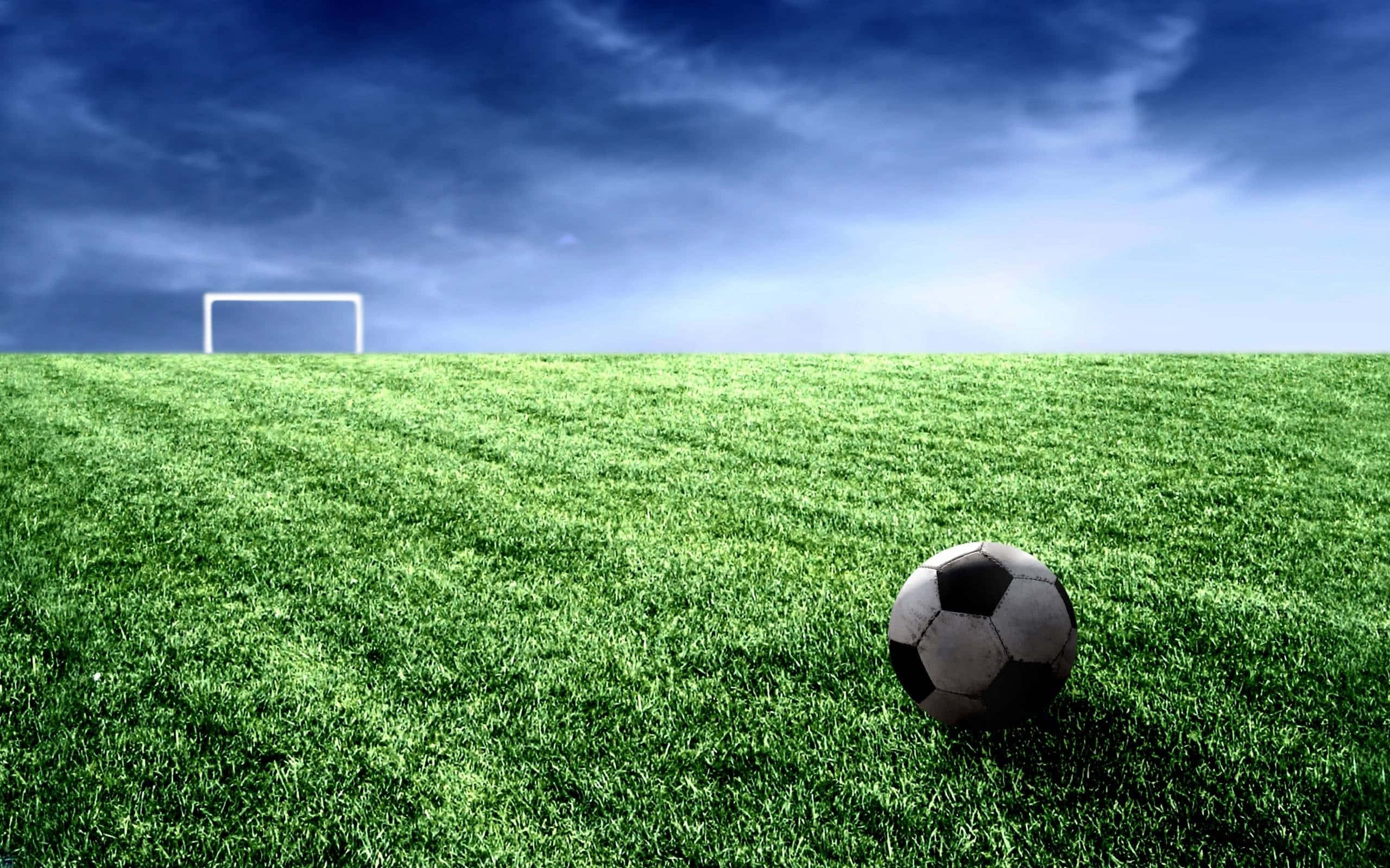 Soccer 4K 桌布 壁紙 — 一個經典的黑白足球放在充滿活力的綠色草地上，遠處有白色的球門柱，背景是戲劇性的藍天。