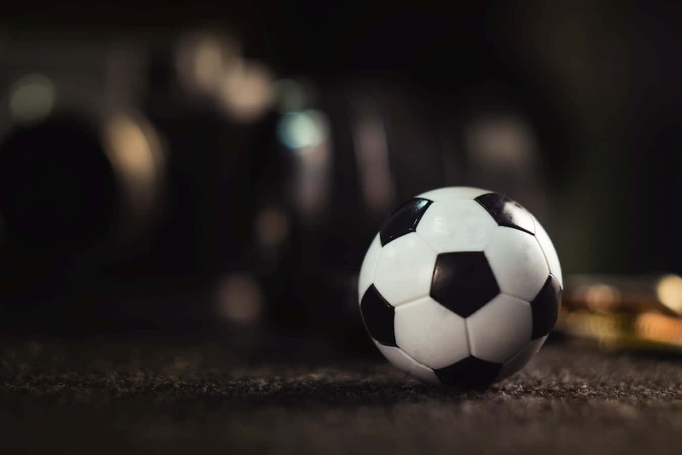 Soccer Ball 桌布 壁紙 — 一個經典的黑白足球放在深色紋理表面上，背景有模糊的健身器材。