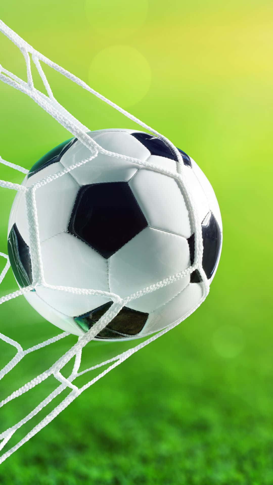 Soccer iPhone 桌布 壁紙 — 一個經典的黑白足球躺在白色網中，背景是充滿活力的綠色模糊背景。