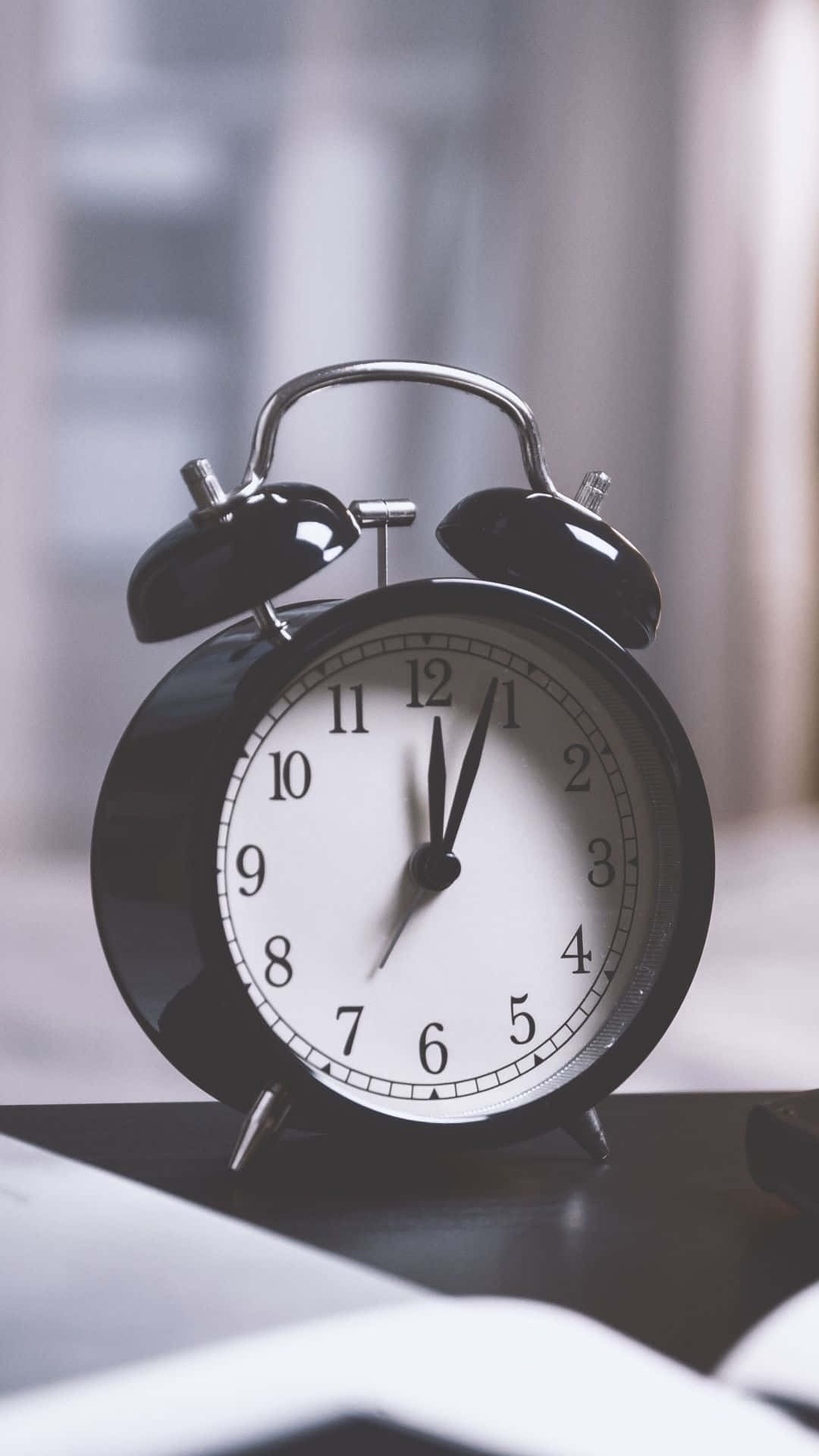 Clock 桌布 壁紙 — 一個經典的黑色鬧鐘帶有鈴鐺，放在桌上顯示12:01，指針準備迎接新的一小時。