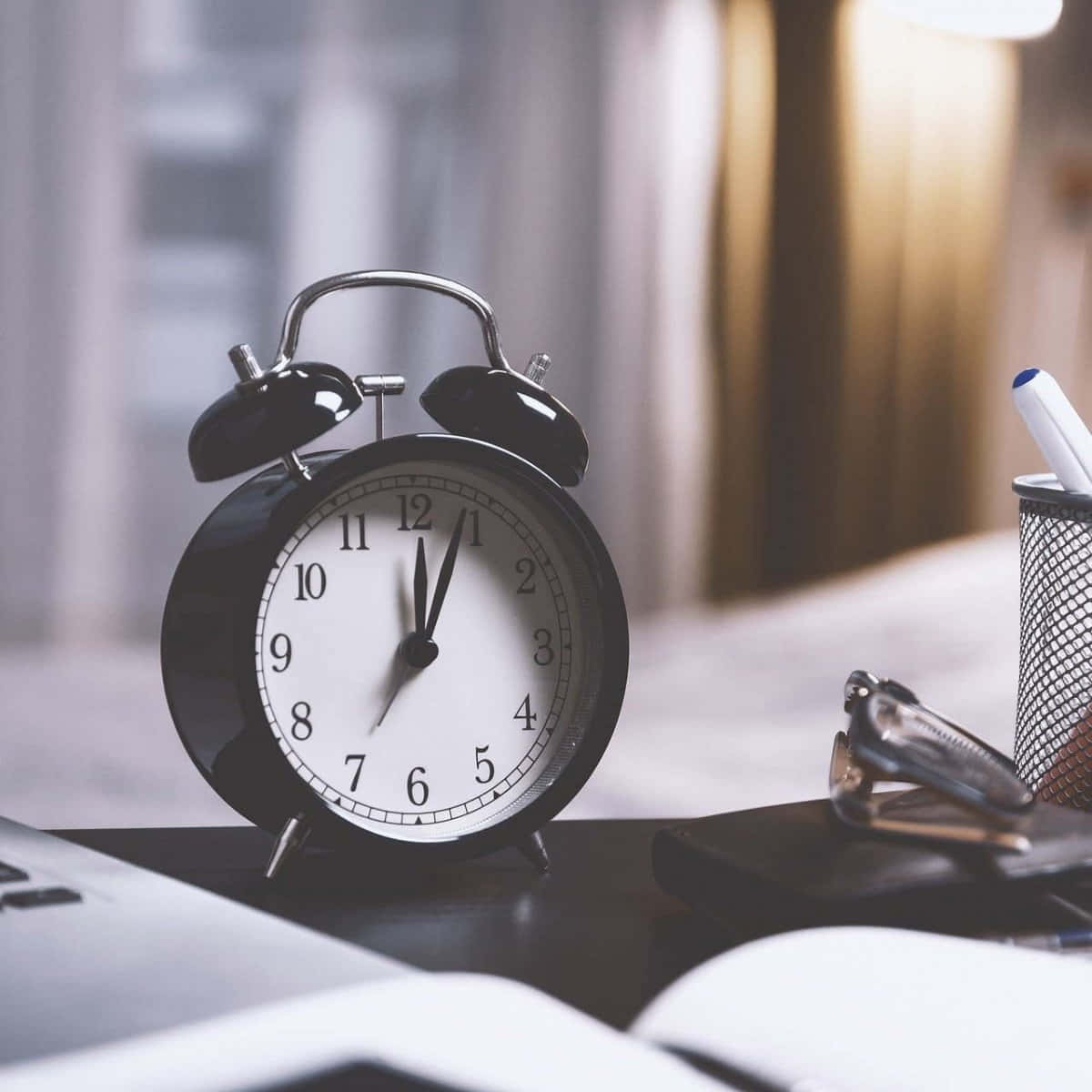 Clock 桌布 壁紙 — 一個經典的黑色鬧鐘放在書桌上，旁邊有眼鏡和筆筒，房間光線柔和。