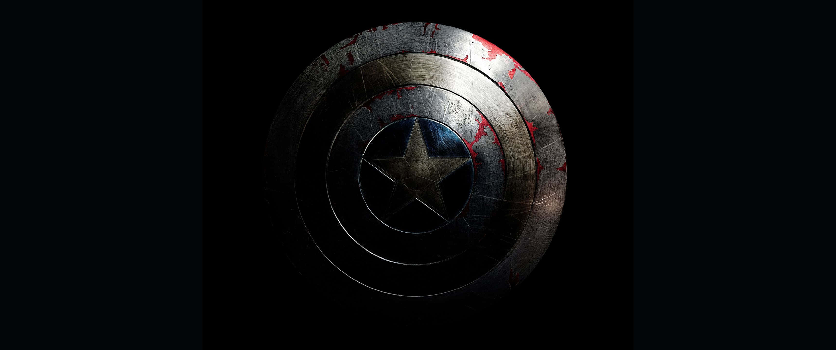 3440x1440p Captain America 桌布 壁紙 — 一個經歷戰鬥、帶有紅色飛濺的美國隊長盾牌，在黑色背景的戲劇性燈光下發光。