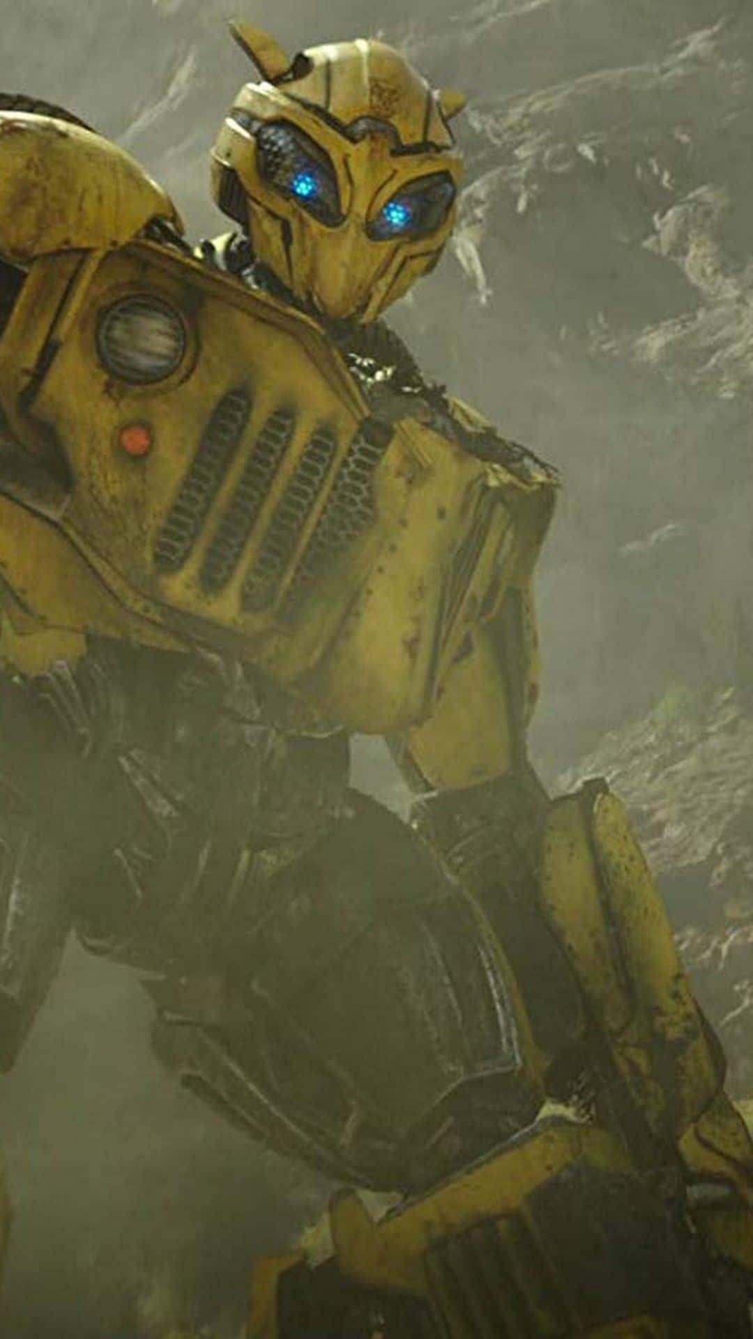 Bumblebee Transformer 桌布 壁紙 — 一個經歷戰鬥磨損的黃色機器人，擁有發光的藍色眼睛，站在岩石地形中，處於塵土飛揚、飽受戰爭摧殘的環境。