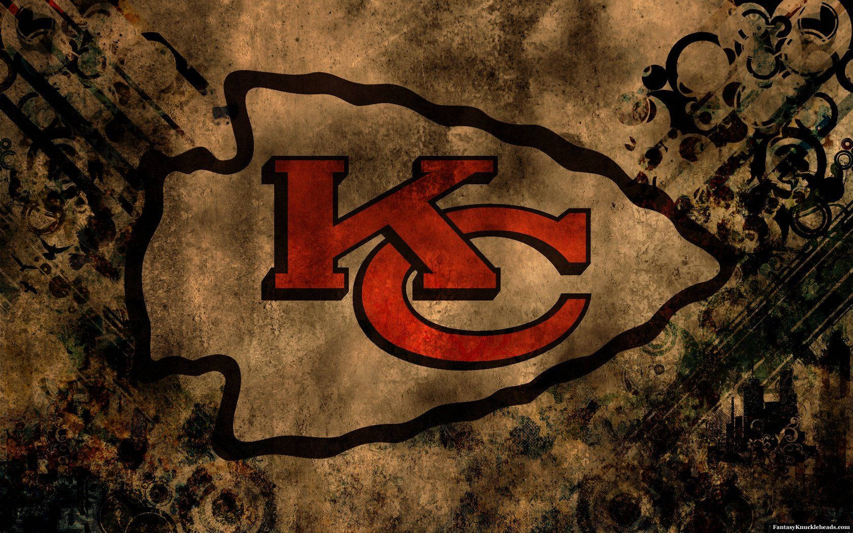 Kc Chiefs 桌布 壁紙 — 一個經風化處理的堪薩斯城酋長隊標誌，以紅色和黑色呈現，置於帶有華麗深色圖案的粗糙紋理背景上。