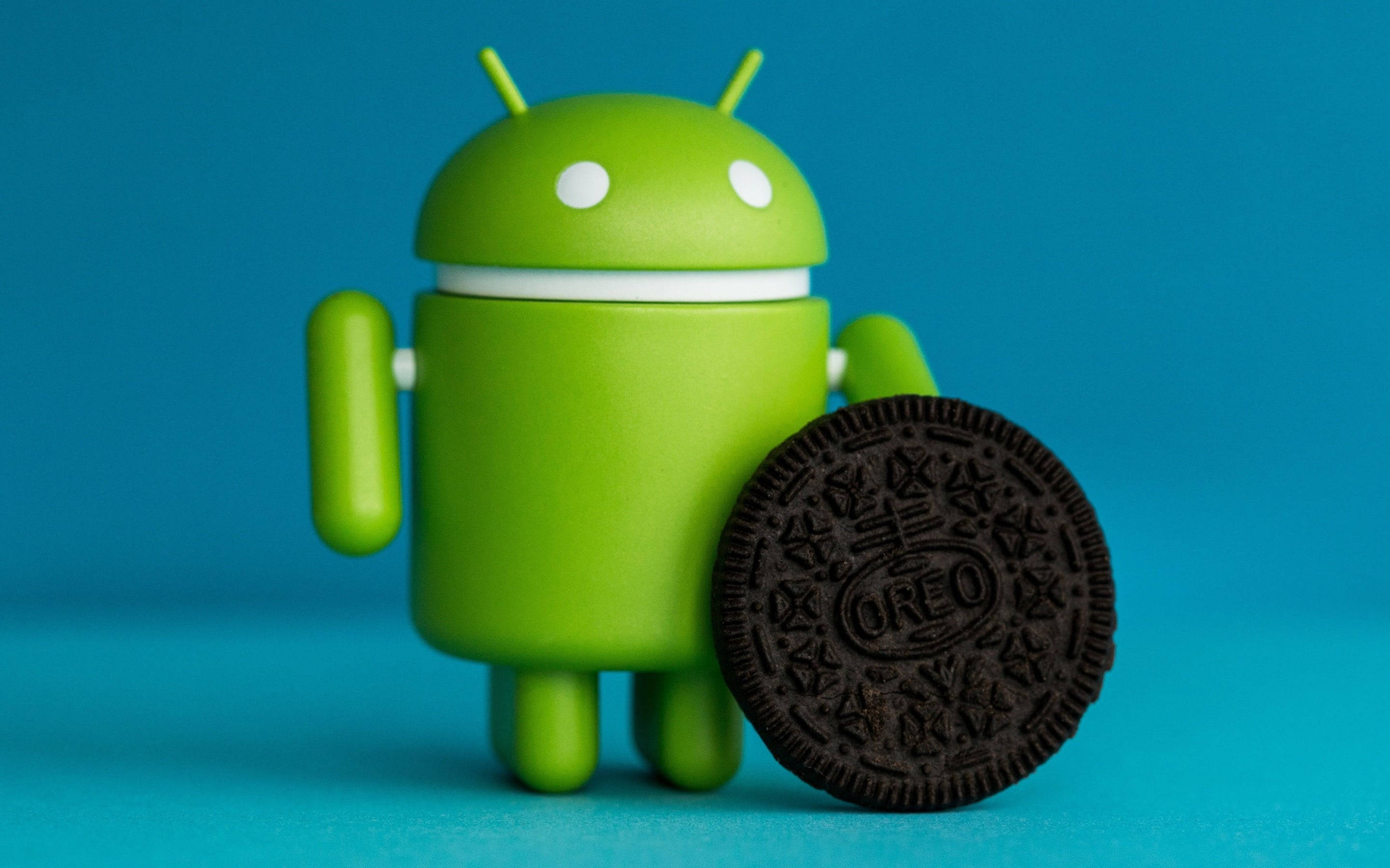 Android Desktop 桌布 壁紙 — 一個綠色Android公仔站在一塊巧克力Oreo餅乾旁邊，背景為純藍色。