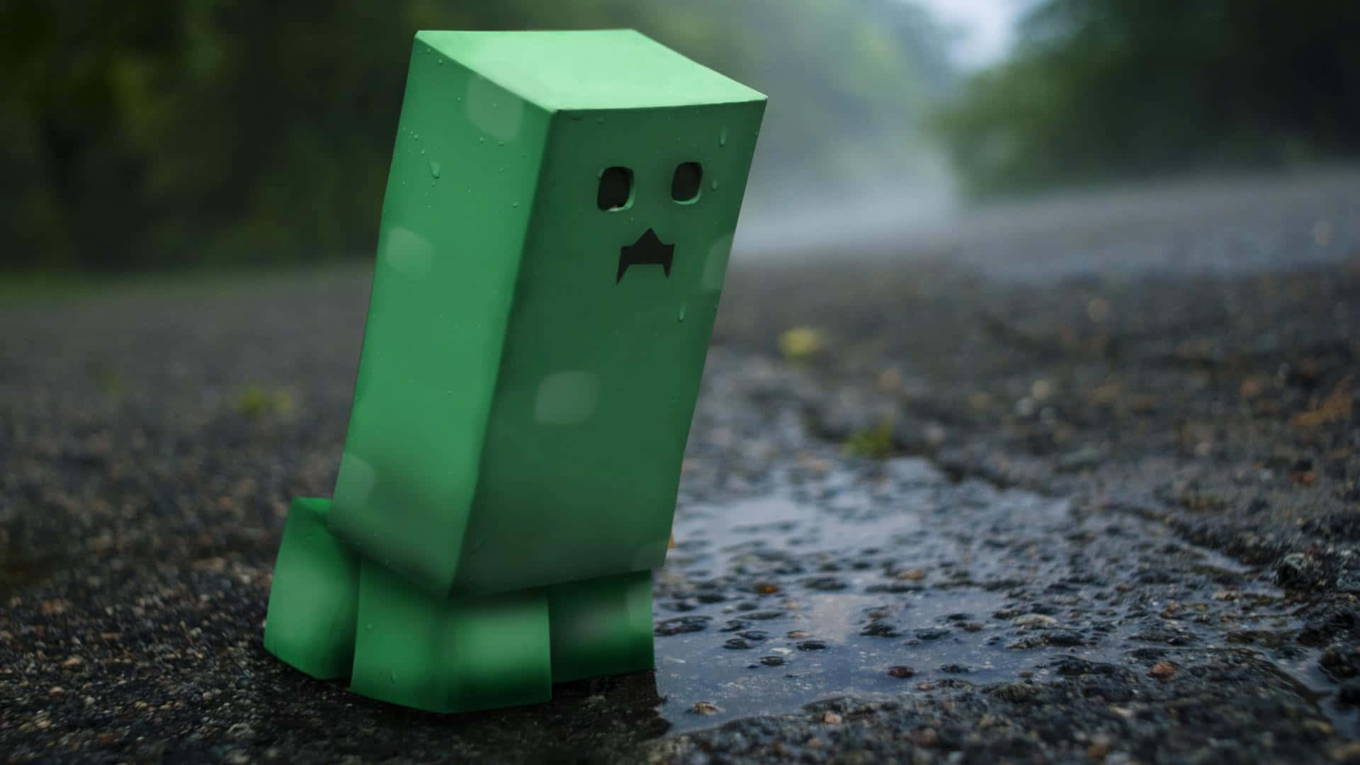 可愛 Minecraft 桌布 壁紙 — 一個綠色Minecraft爬行者在霧雨暴風中獨自站在濕漉漉的瀝青路上，背景是模糊的森林。