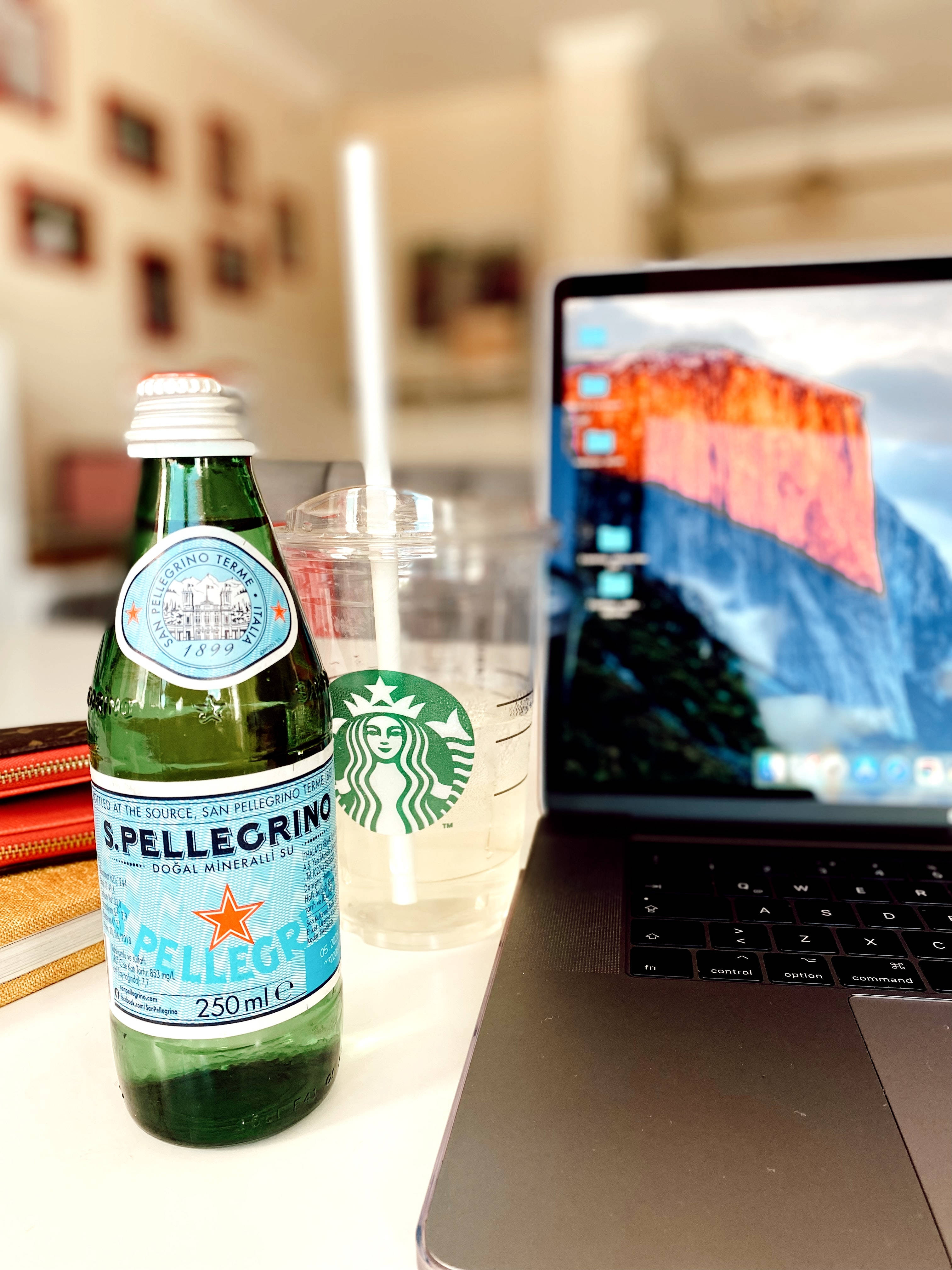 aesthetic tumblr laptop 桌布 壁紙 — 一個綠色S Pellegrino瓶子和一個Starbucks杯放在一張白色桌子上，旁邊是一部打開的筆記型電腦，顯示著山脈壁紙。