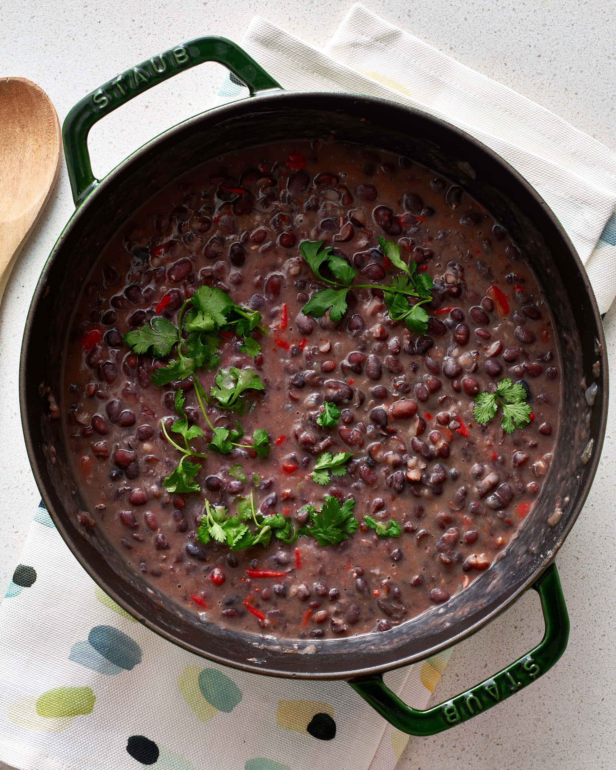 Black Bean Soup 桌布 壁紙 — 一個綠色Staub鍋盛滿豐富的黑豆，配上新鮮香菜和紅椒，放在圖案布上。