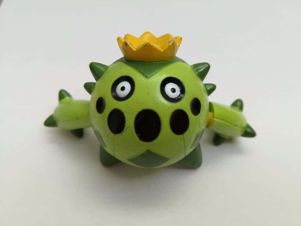 Cacnea 桌布 壁紙 — 一個綠色帶刺的玩具生物，戴著黃色皇冠和黑色斑點，坐在純白色背景前。