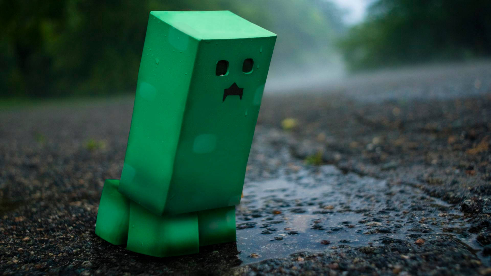 Creeper 桌布 壁紙 — 一個綠色方塊狀的爬行者獨自站在潮濕的瀝青路上，天空多雲有霧。