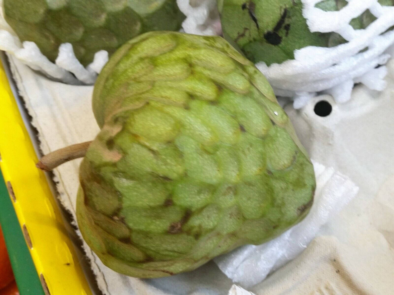 iPhone 桌布 壁紙 — 一個綠色有鱗片的刺果番荔枝果實特寫，放在市場攤位的白色發泡膠托盤上。