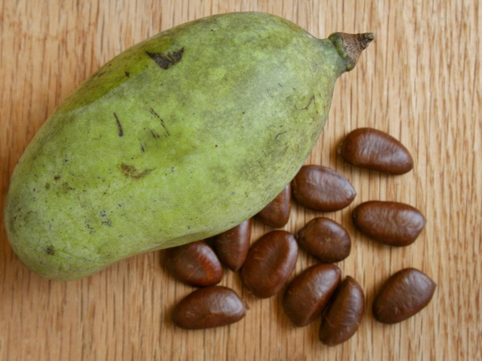 Fruit 桌布 壁紙 — 一個綠色泡泡果帶有棕色種子，放在淺色木質表面上。