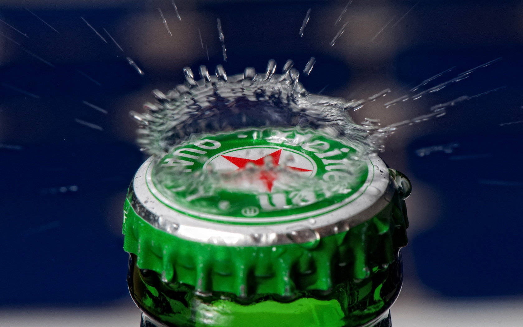 Drink 桌布 壁紙 — 一個綠色海尼根啤酒瓶蓋爆開，液體動態飛濺，背景是深藍色的特寫。