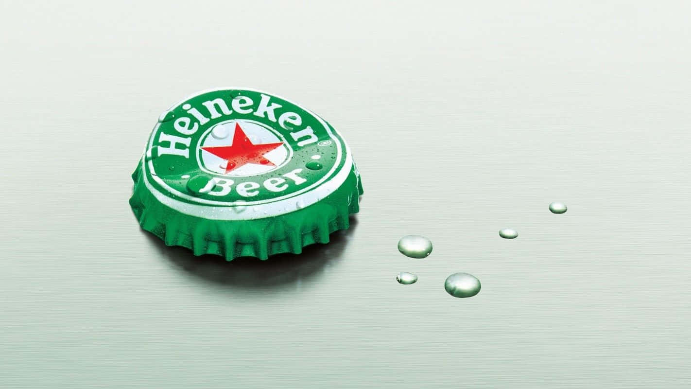 Heineken 桌布 壁紙 — 一個綠色海尼根啤酒蓋放在拉絲金屬表面上，旁邊有冷凝水滴。