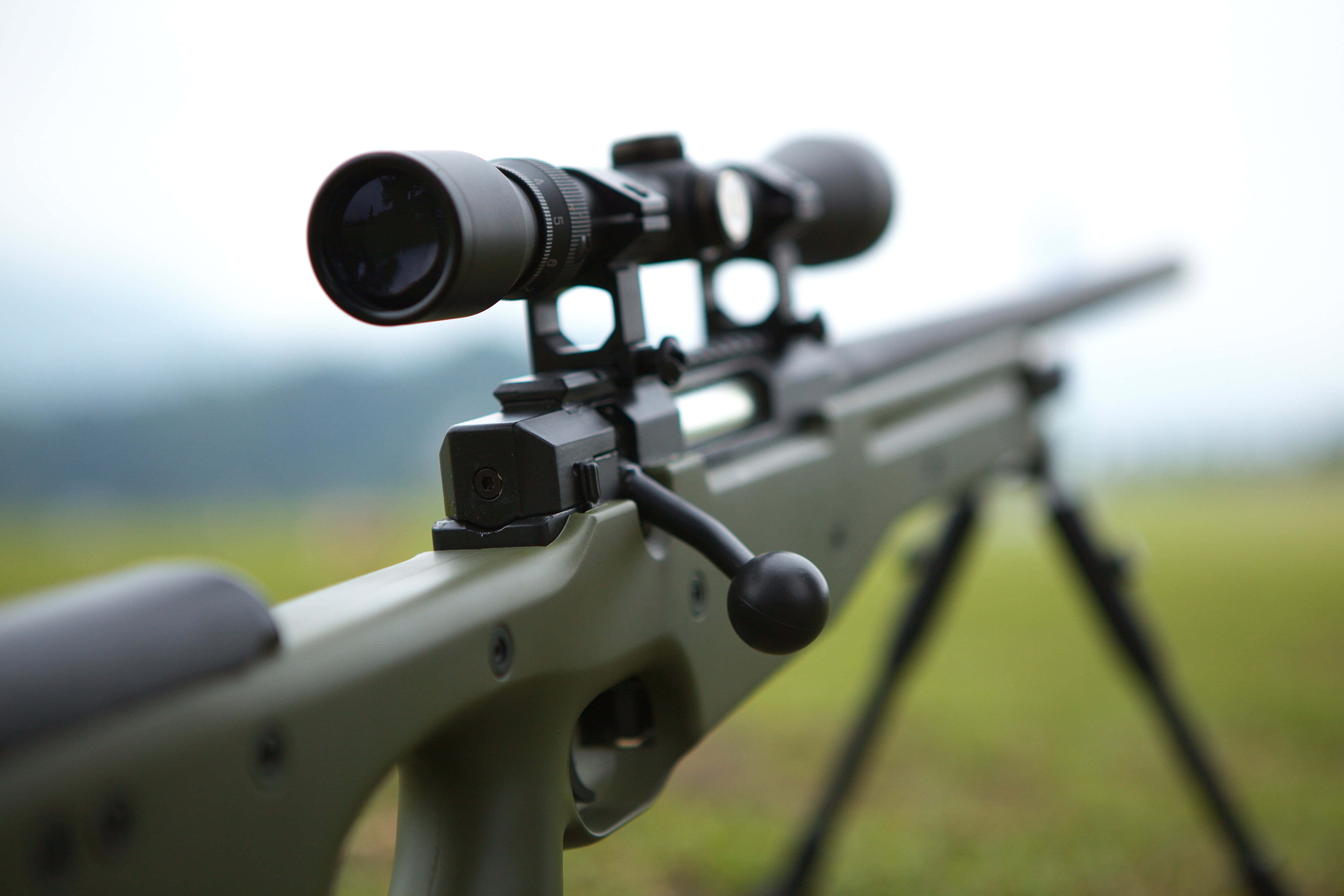 Rifle 桌布 壁紙 — 一個綠色狙擊步槍的特寫，帶有瞄準鏡安裝在三腳架上，背景是模糊的草地。