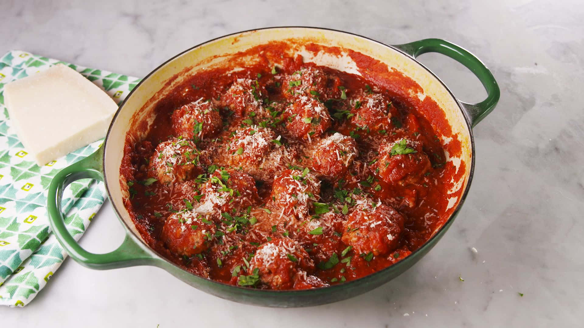 Red Sauce 桌布 壁紙 — 一個綠色琺瑯鑄鐵煎鍋，裝滿了在濃郁番茄醬中慢煮的肉丸，上面撒上新鮮歐芹和磨碎的起司。