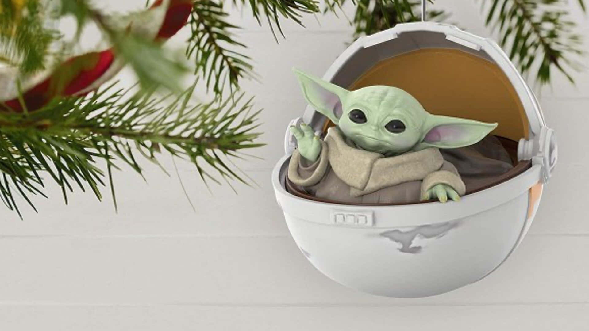Christmas Ornament 桌布 壁紙 — 一個綠色的Baby Yoda公仔坐在一個掛在松樹枝上的白色豆莢裝飾裡面。