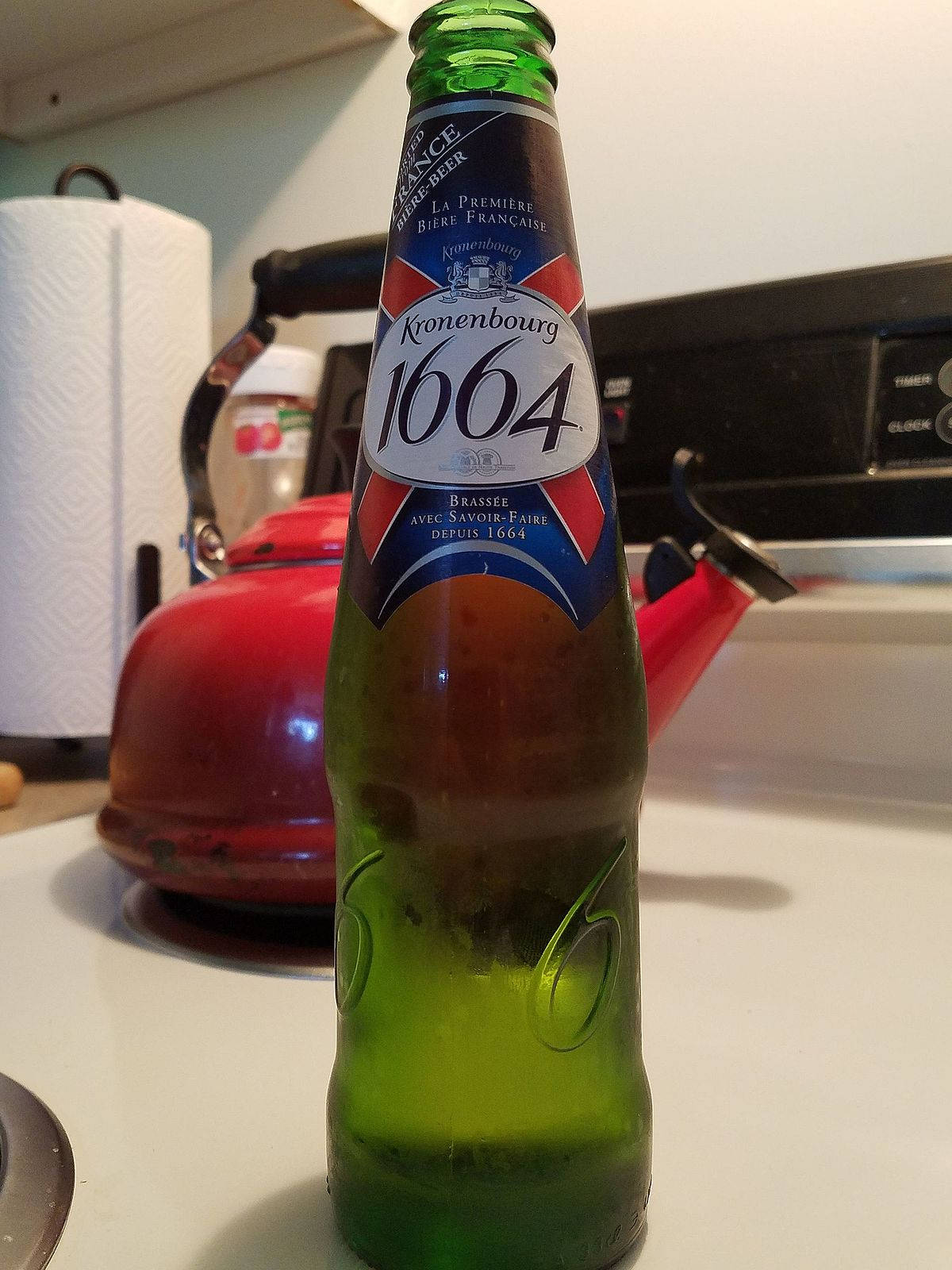 Beer 桌布 壁紙 — 一個綠色的Kronenbourg 1664啤酒瓶放在白色廚房檯面上，旁邊有一個紅色水壺。