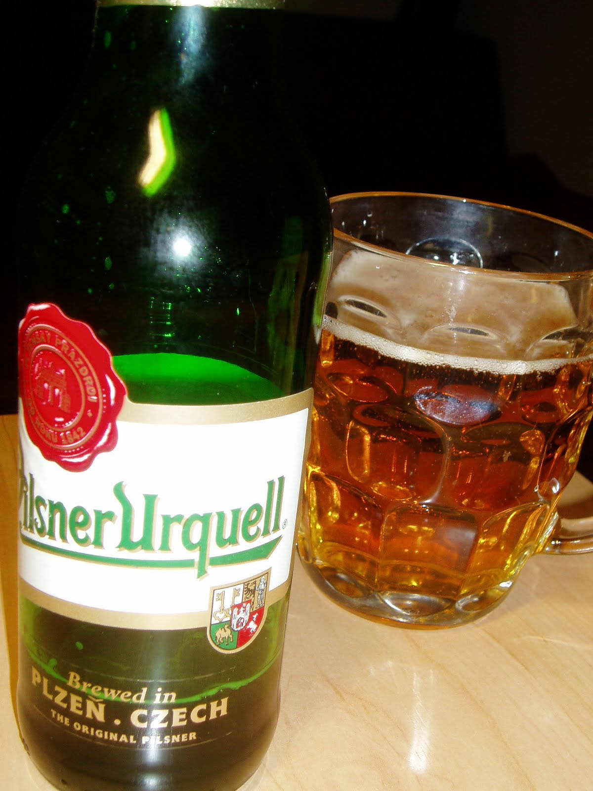 glass 桌布 壁紙 — 一個綠色的Pilsner Urquell啤酒瓶放在木桌上，旁邊有一杯琥珀色啤酒加冰。