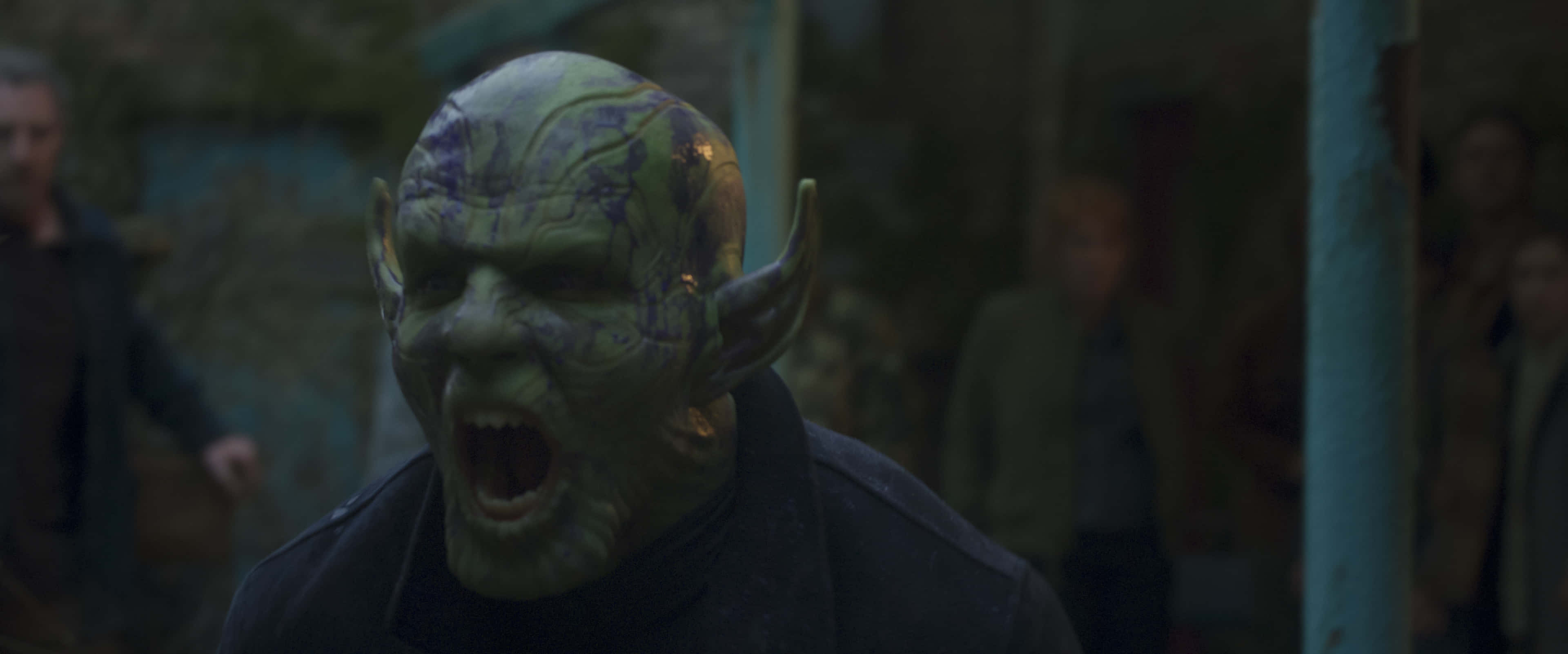 Skrulls 桌布 壁紙 — 一個綠色皮膚、帶有紫色斑紋和尖耳朵的外星人在昏暗的城市小巷中猛烈尖叫。