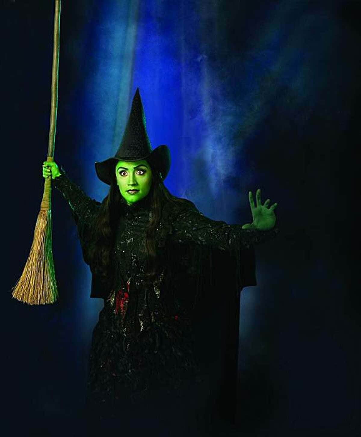 Evil Witch 桌布 壁紙 — 一個綠色皮膚、戴黑色尖帽的女巫，在深藍色煙霧背景前拿著掃帚。