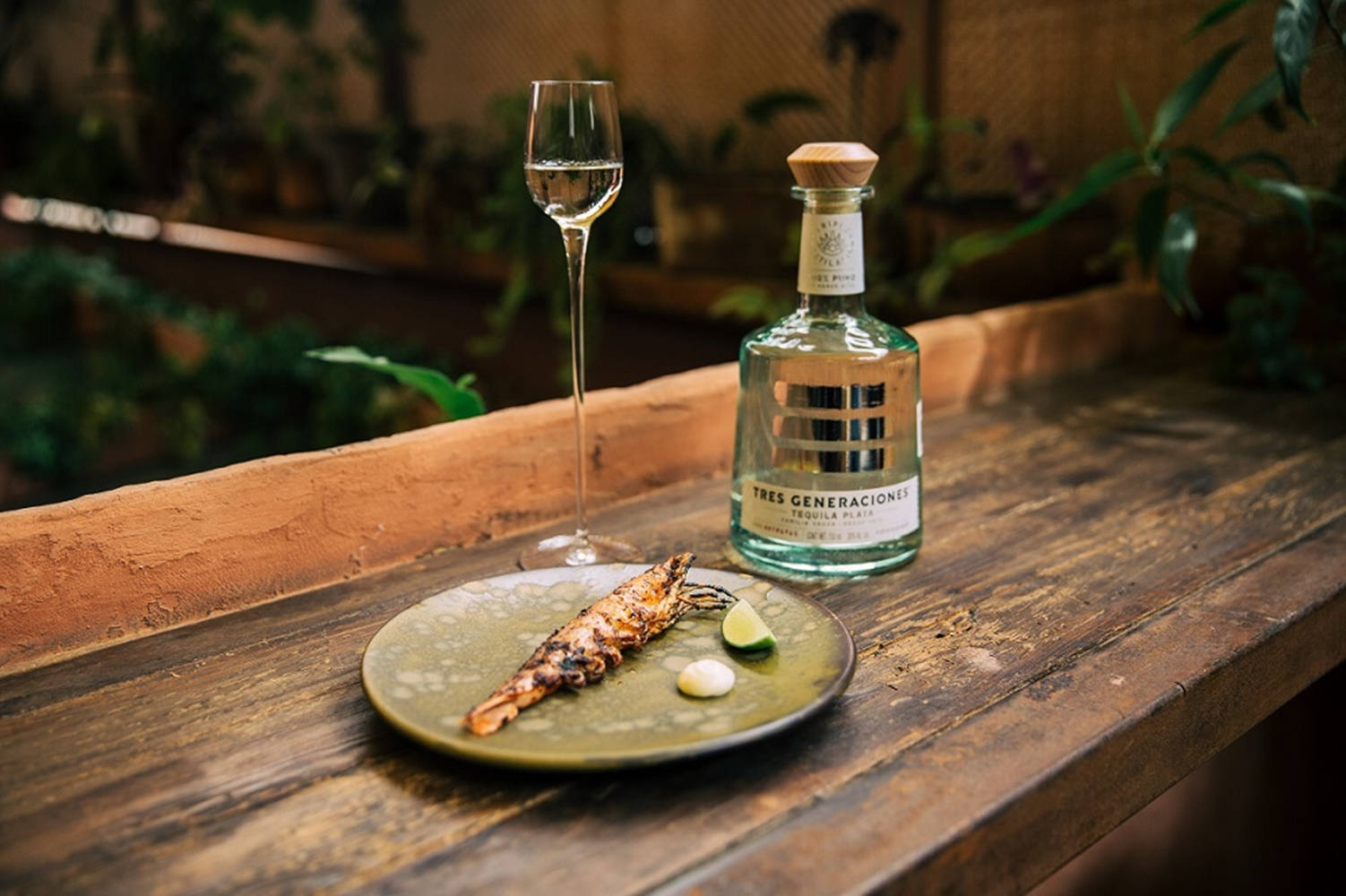alcohol 桌布 壁紙 — 一個綠色盤子上的烤蝦搭配萊姆和奶油，旁邊有龍舌蘭酒瓶和杯子，放在鄉村風木製吧檯上。