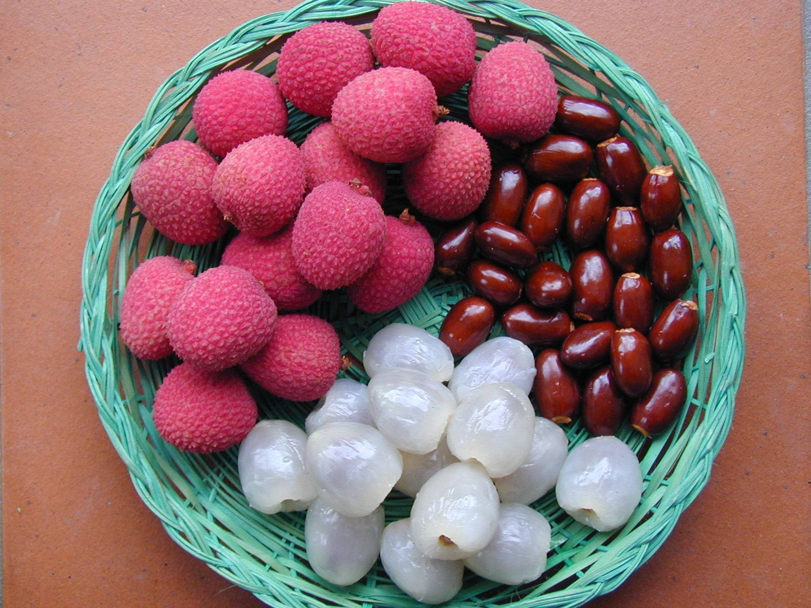 Fruit 桌布 壁紙 — 一個綠色編織籃子裡裝著鮮豔的粉紅色荔枝、有光澤的紅色椰棗和半透明的白色龍眼，整齊地排列在赤陶表面上。