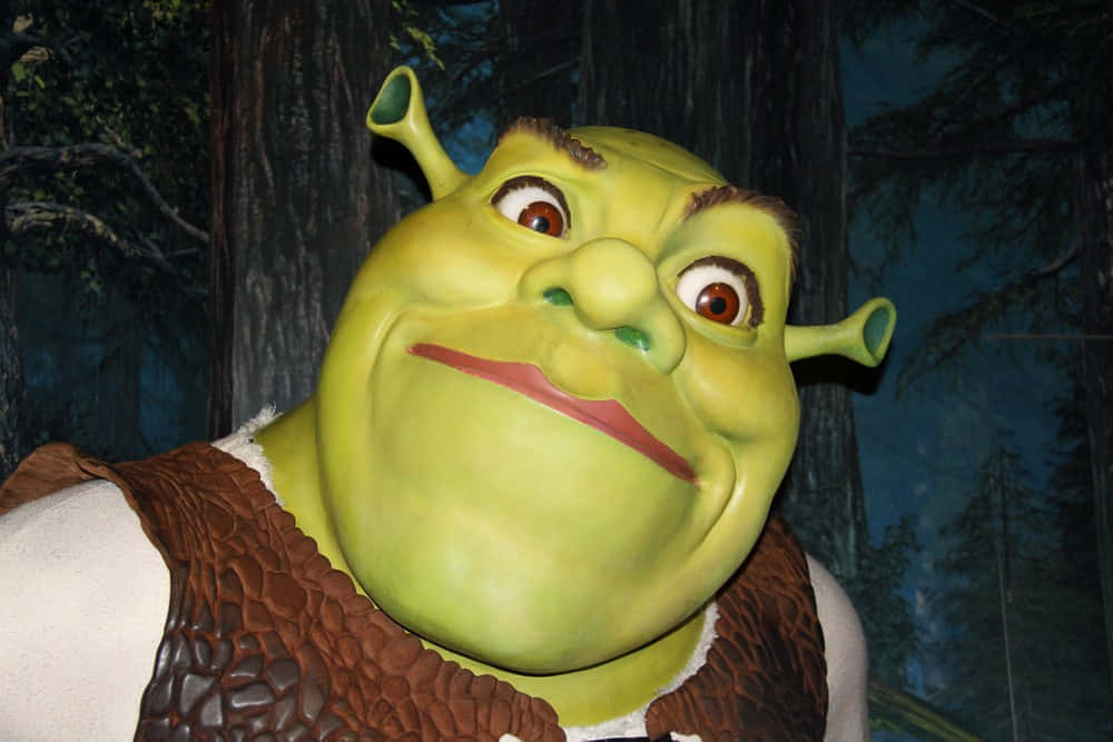 Funny Shrek 桌布 壁紙 — 一個綠色食人魔的特寫，有大耳朵和咧嘴笑，穿著棕色背心，背景是黑暗的森林。