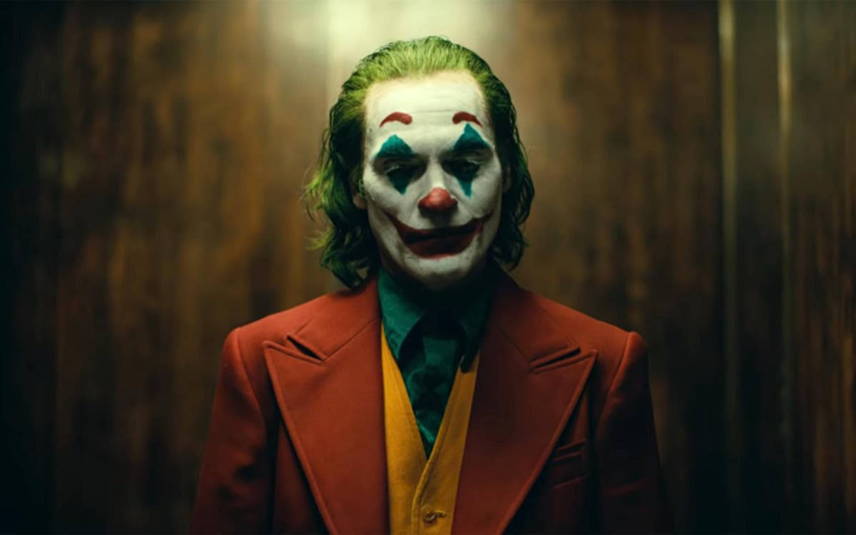 Why So Serious Joker 桌布 壁紙 — 一個綠髮小丑妝的男人在昏暗的木製電梯內穿著紅色西裝，眼神銳利地凝視。
