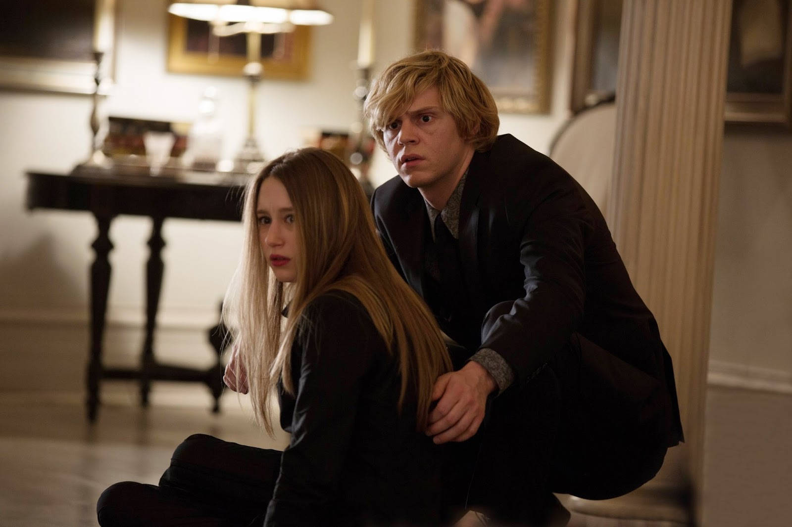 Tate Langdon 桌布 壁紙 — 一個緊張的場景，兩個年輕人蹲在燈光昏暗的華麗房間裡，表情恐懼而警覺。