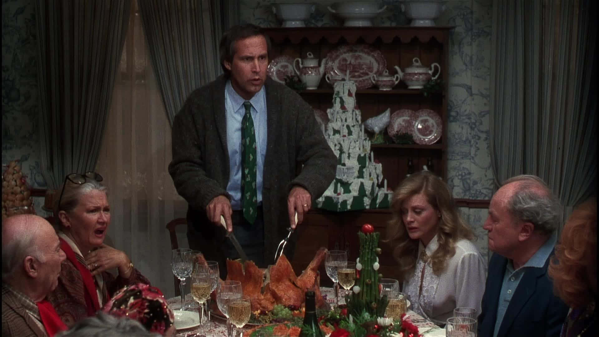Christmas Vacation 桌布 壁紙 — 一個緊張的家庭晚餐場景，一名男子正在切火雞，而其他人則表現出震驚和擔憂。