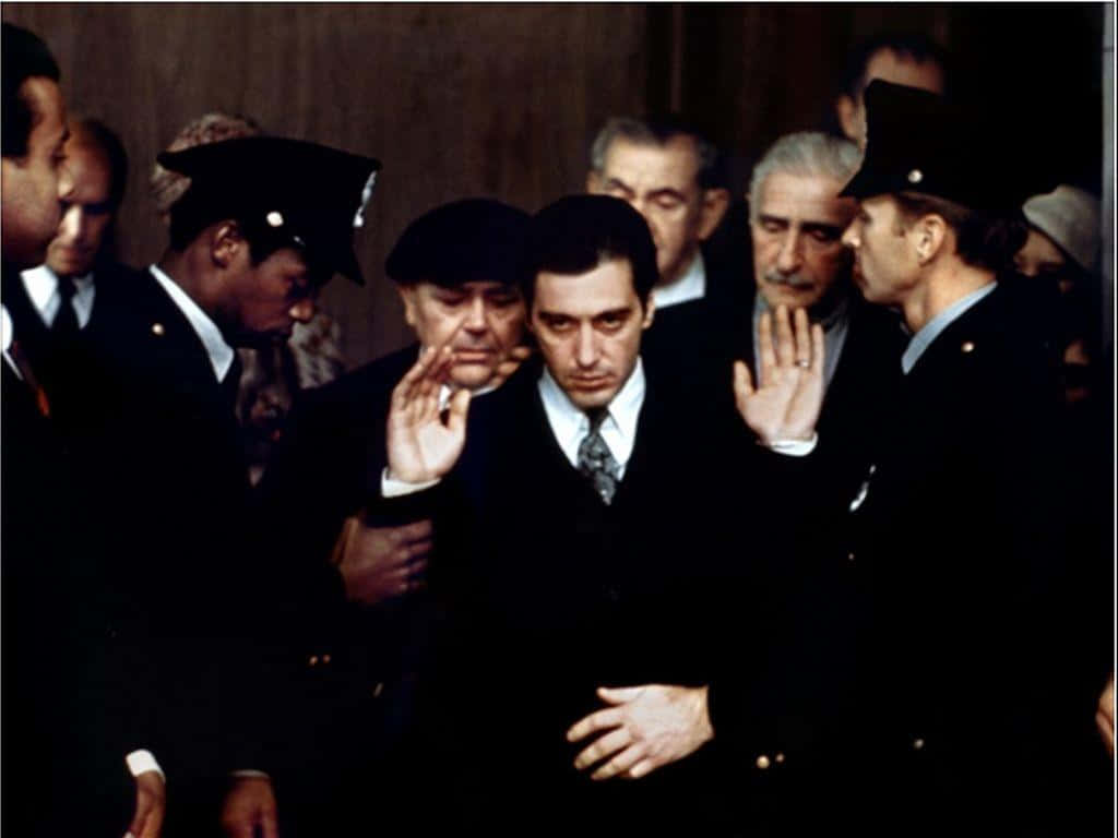 The Godfather 桌布 壁紙 — 一個緊張的法庭場景，中間有一位穿西裝的男子，被穿制服的警員和表情嚴肅的男子包圍。