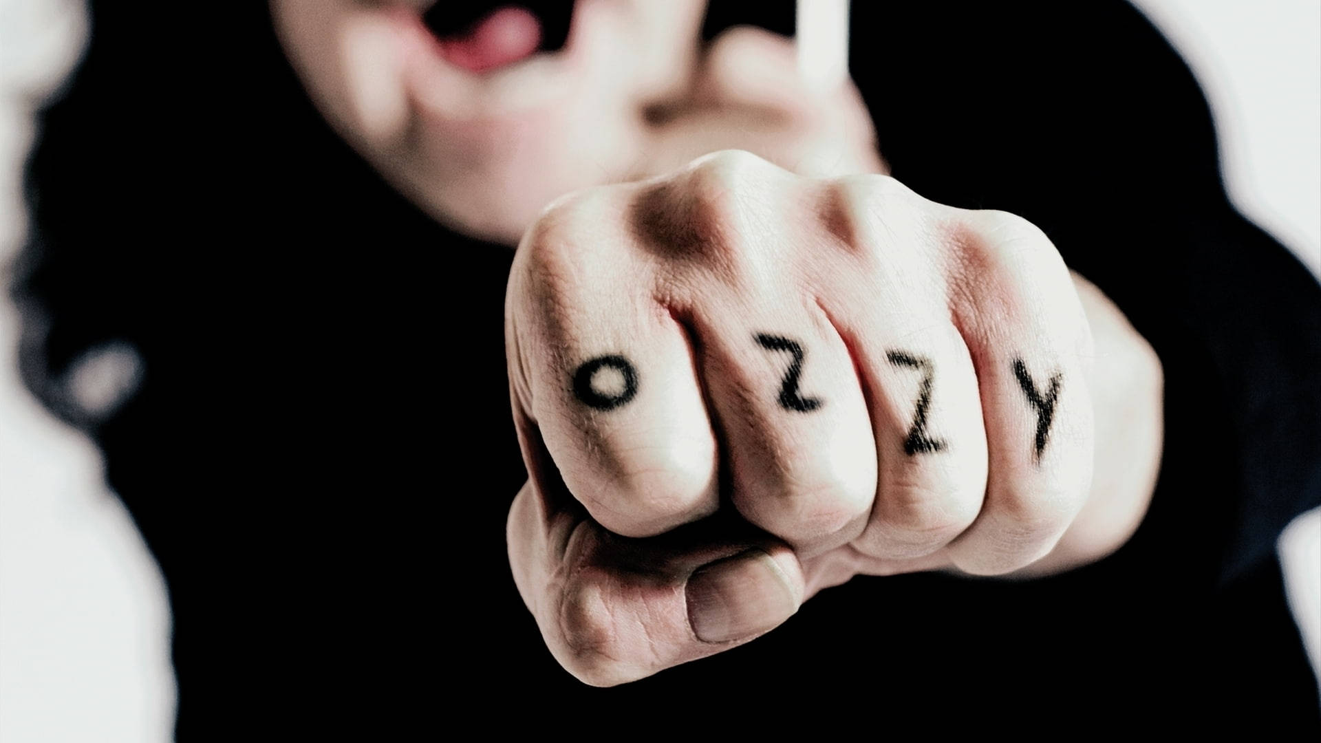 Ozzy Osbourne 桌布 壁紙 — 一個緊握拳頭的特寫，拳頭上寫有「OZZY」字樣，由一名身穿深色襯衫的人向前伸出。