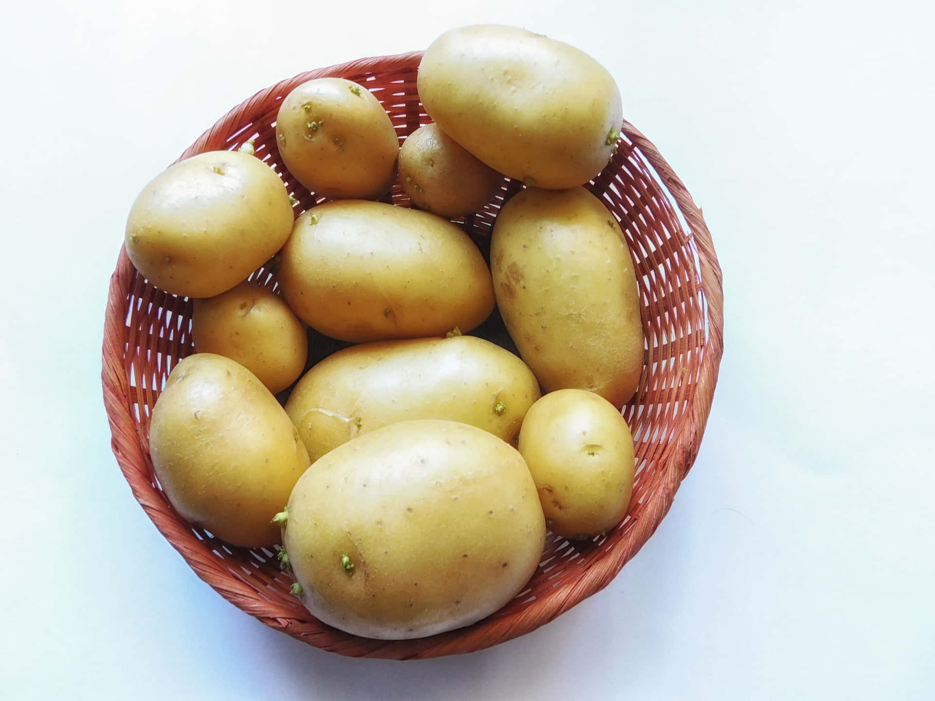 Potatoes 壁紙 — 一個編織的棕色籃子裡裝著一堆光滑的黃色馬鈴薯，背景是明亮的白色。